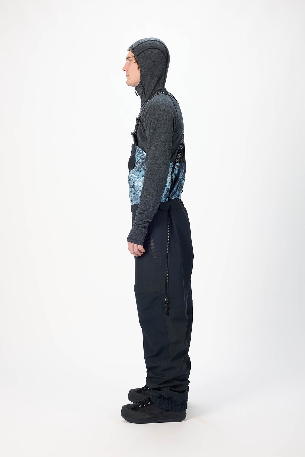 Person wearing a dark gray jacket and black snow pants with a hood on a white background