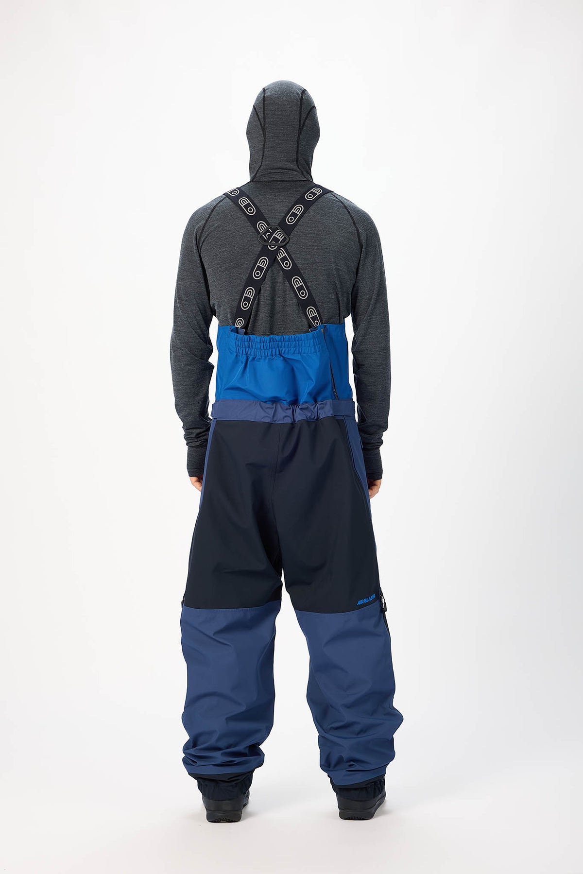 Person wearing a gray hoodie and blue snow pants with a backpack on a white background