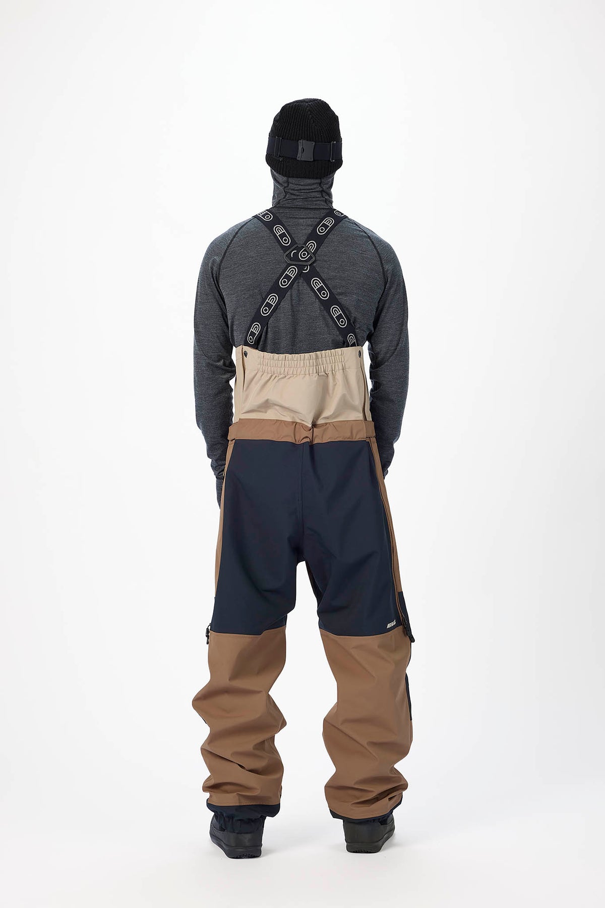 Person wearing a gray jacket, navy pants, and brown pants with suspenders on a white background