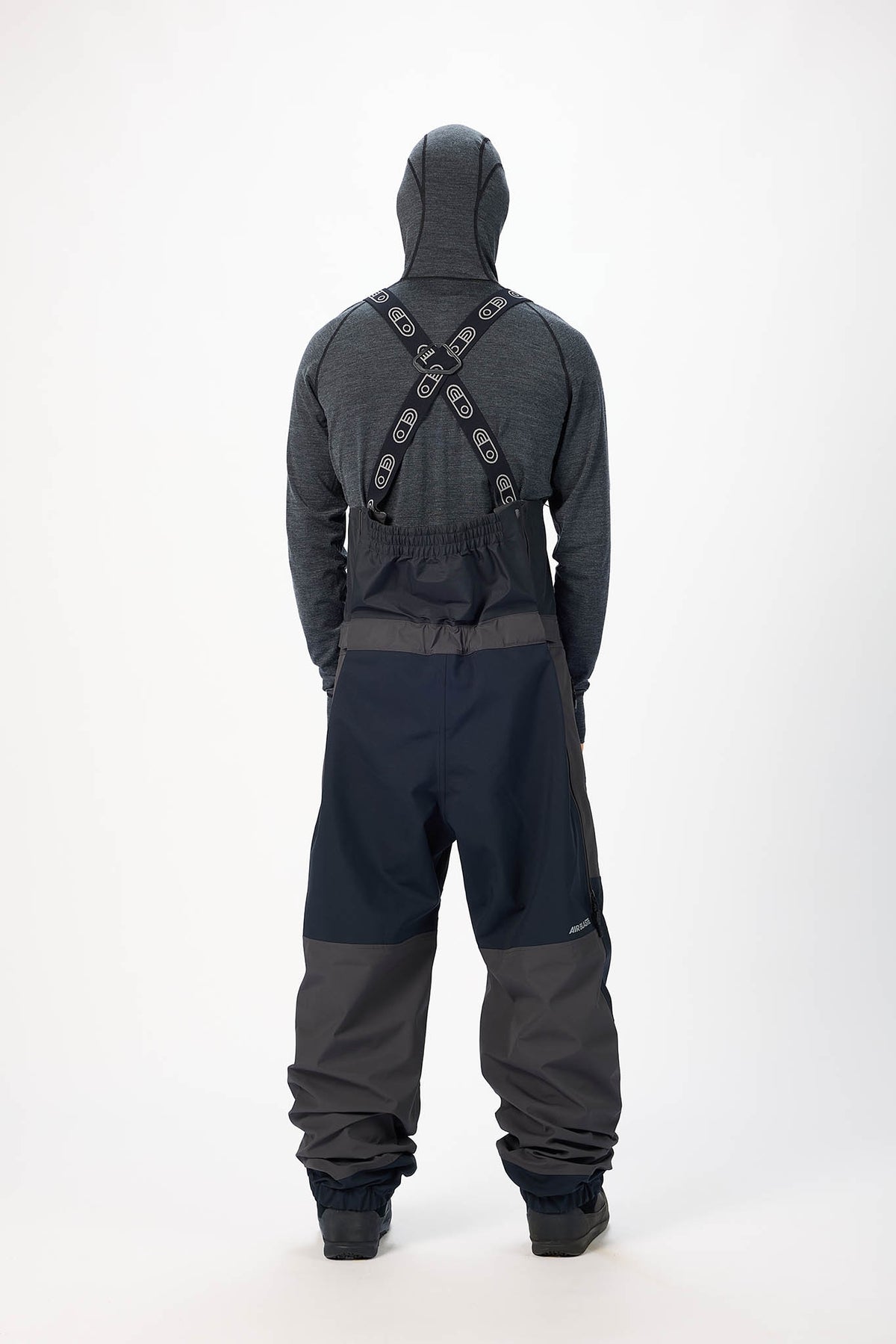 Person wearing a gray and black snowmobile suit with a hood and suspenders on a white background