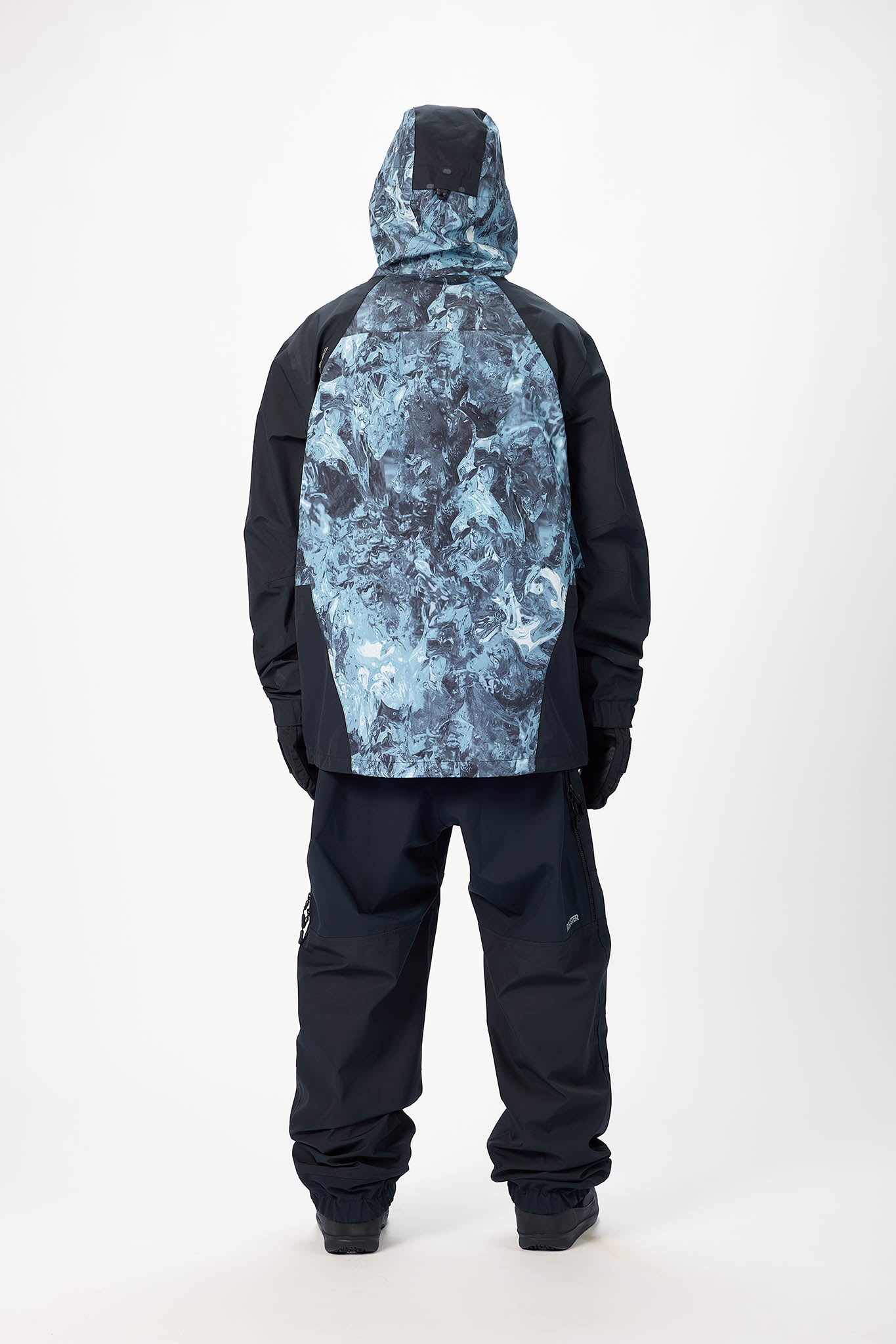 Person wearing a black snowsuit with a blue camouflage pattern on the back against a white background