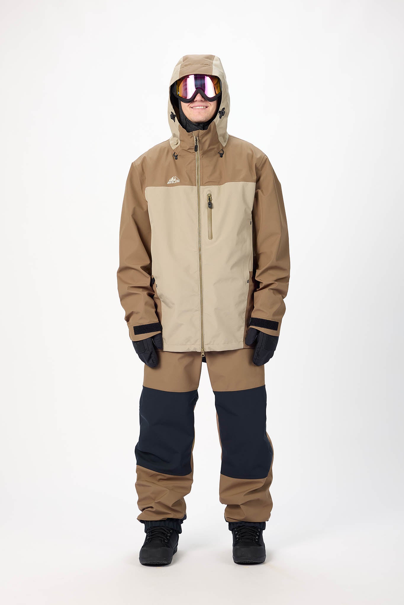 Person wearing a brown and beige snowsuit with goggles on a white background