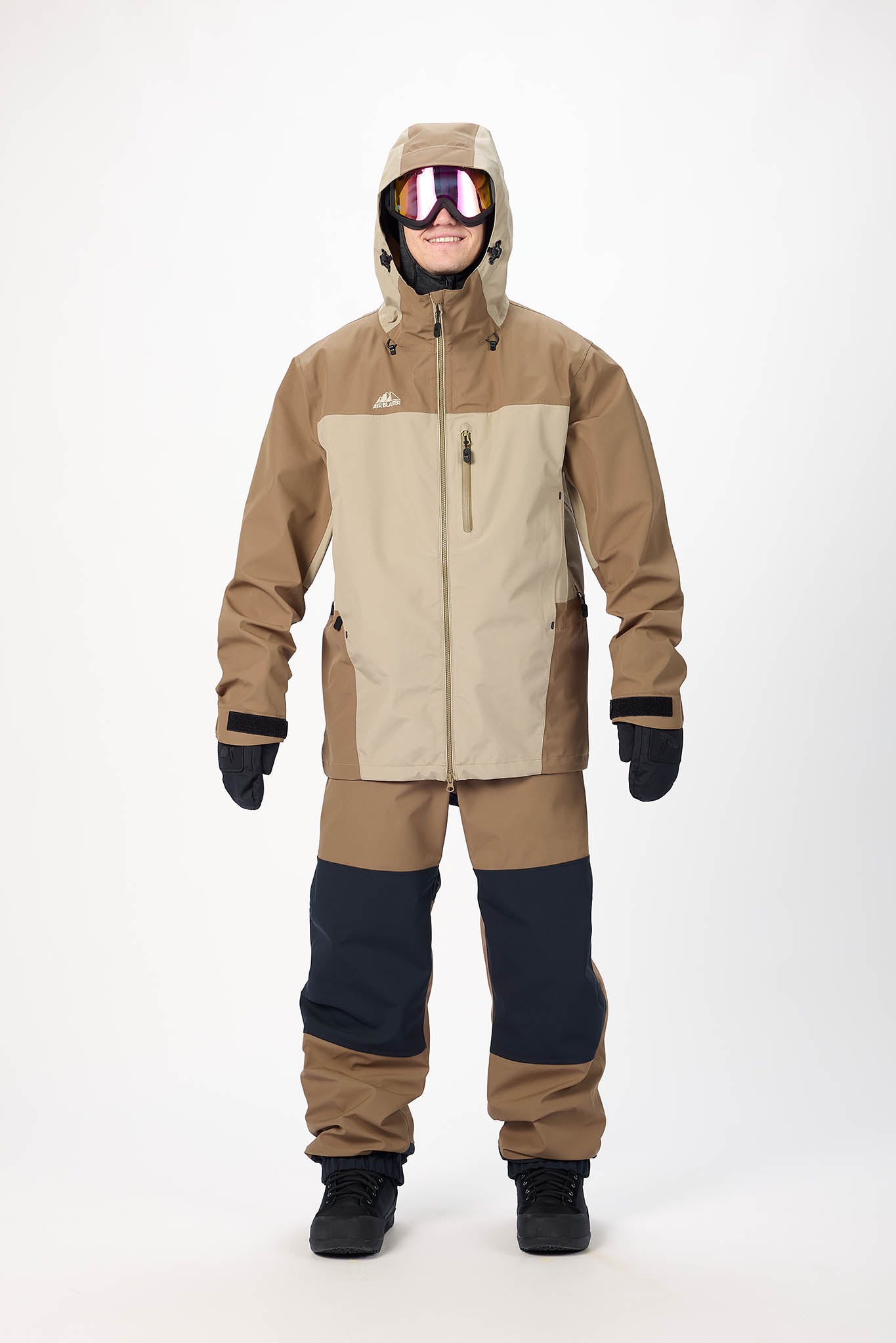 Person wearing a brown and beige snowsuit with goggles on a white background