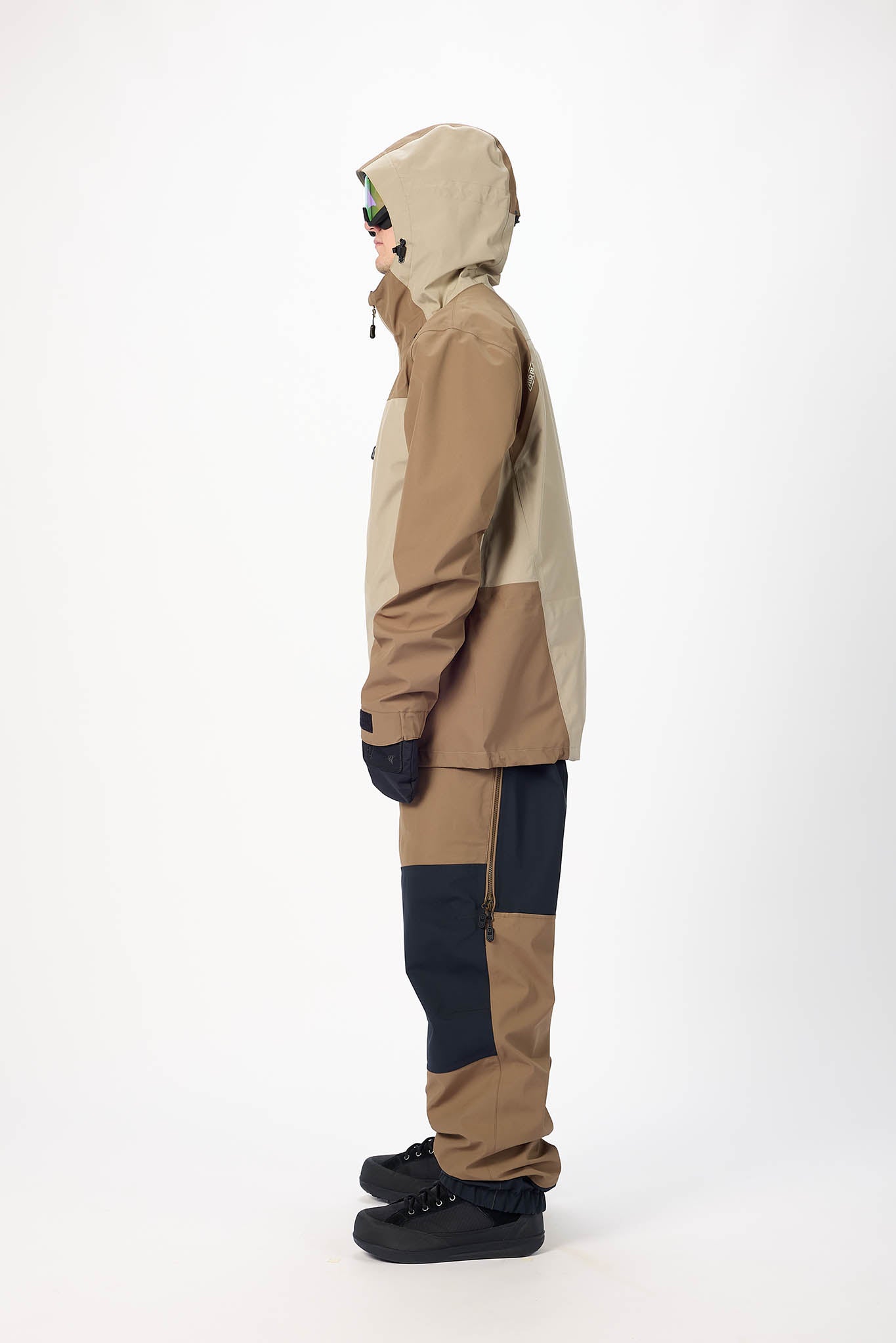 Person wearing a beige and navy jacket with black pants on a white background