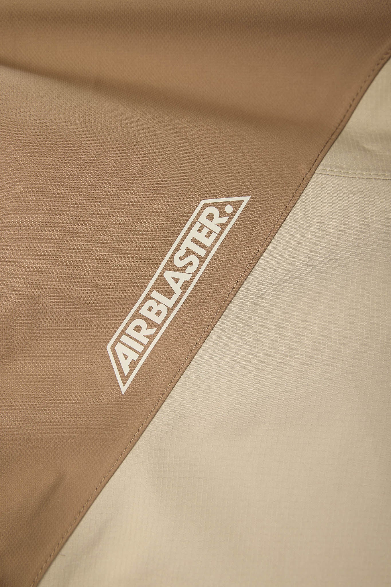 Close-up of AIRBLASTER logo on a brown and beige fabric background