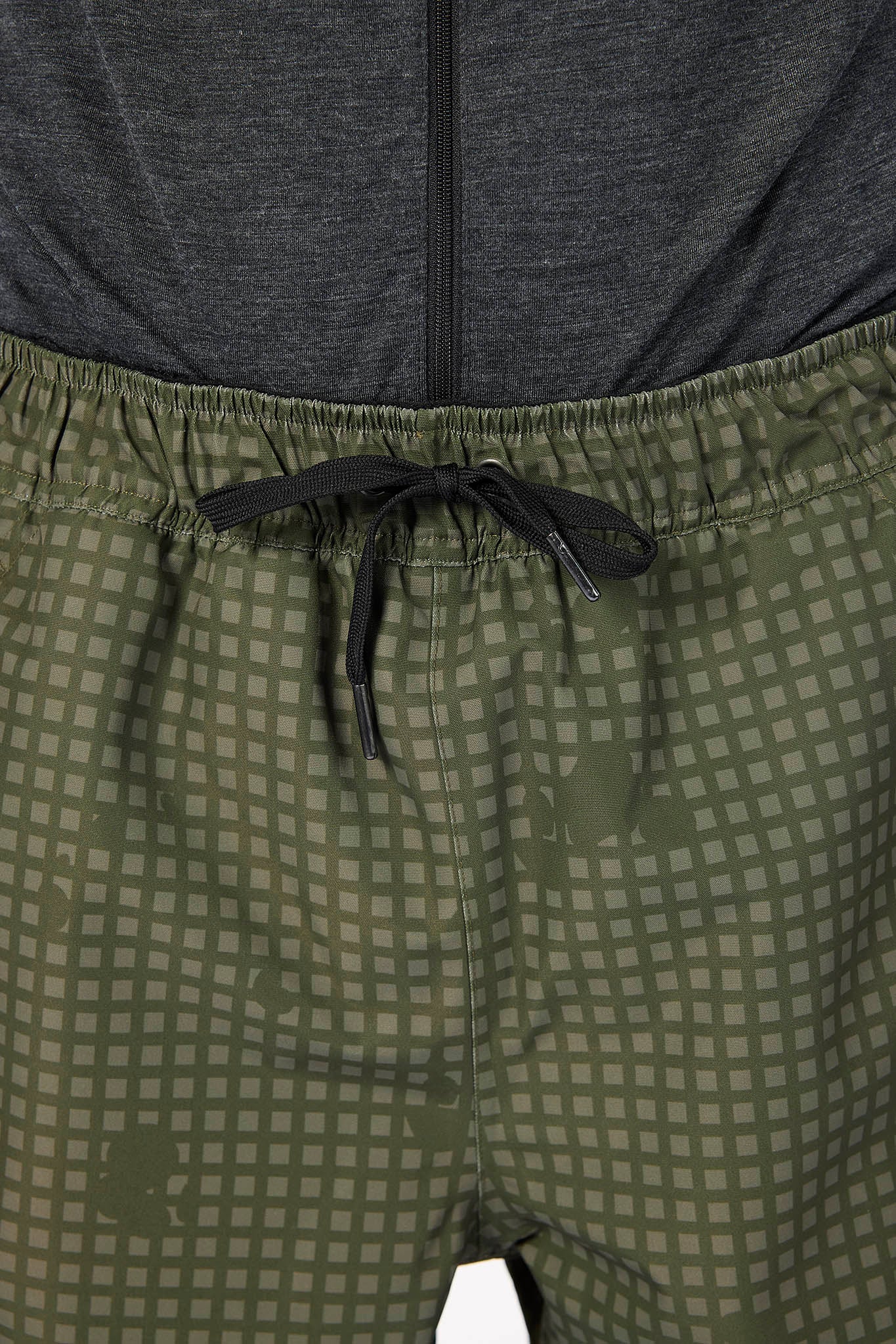 Close-up of olive green patterned shorts with a black drawstring waistband, shown with a dark gray top at the top.