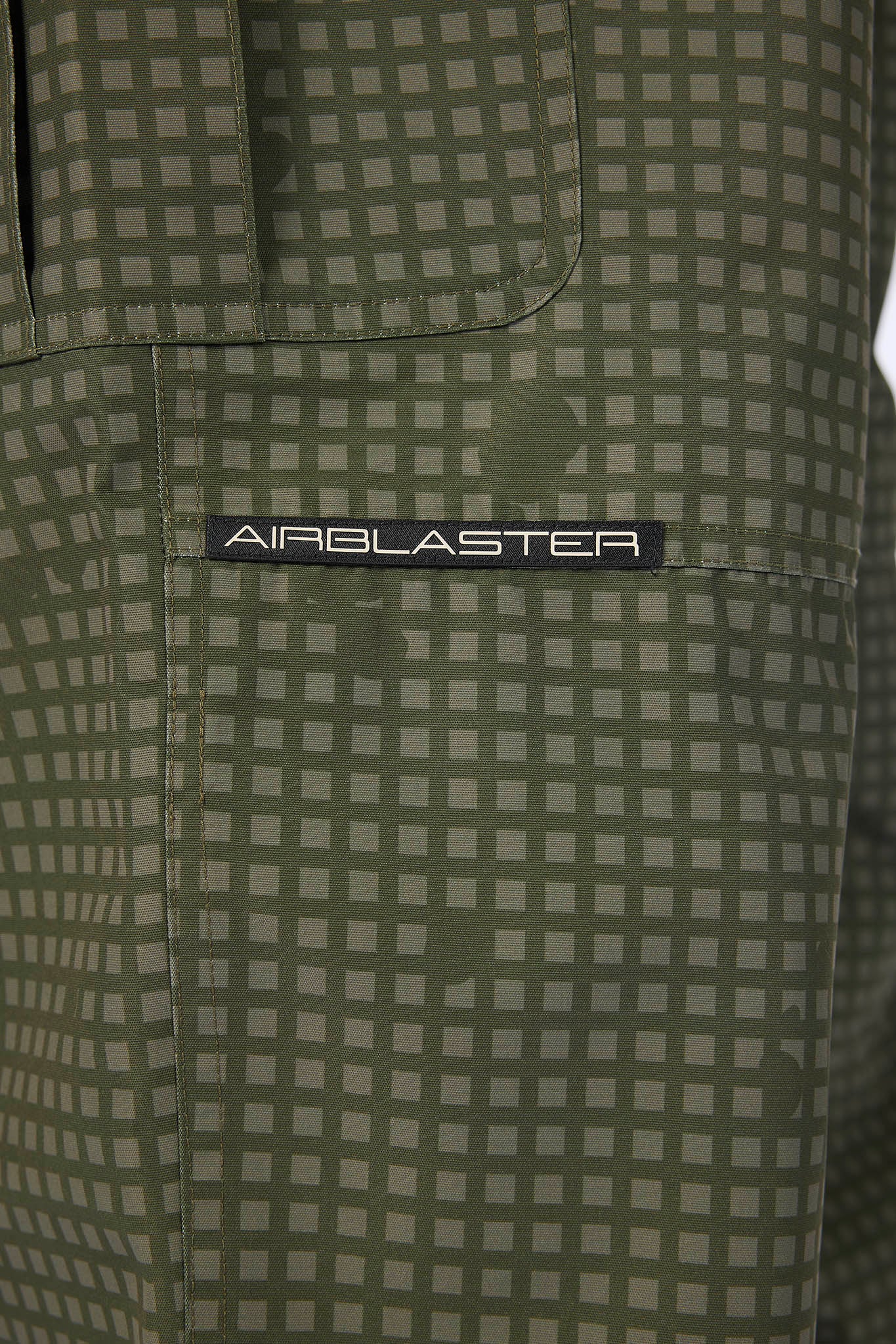 Close-up of olive green patterned fabric with a black rectangular patch reading AIRBLASTER in white text.