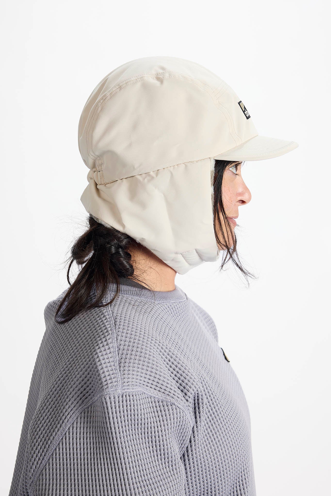 A woman in profile wearing a one outdoor sun hat with a built-in neck flap and visor, set against a plain white background.