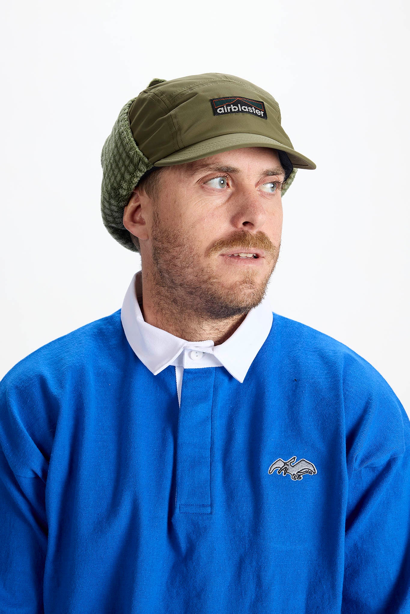 A man wearing an olive green 5-panel cap with ear flaps
