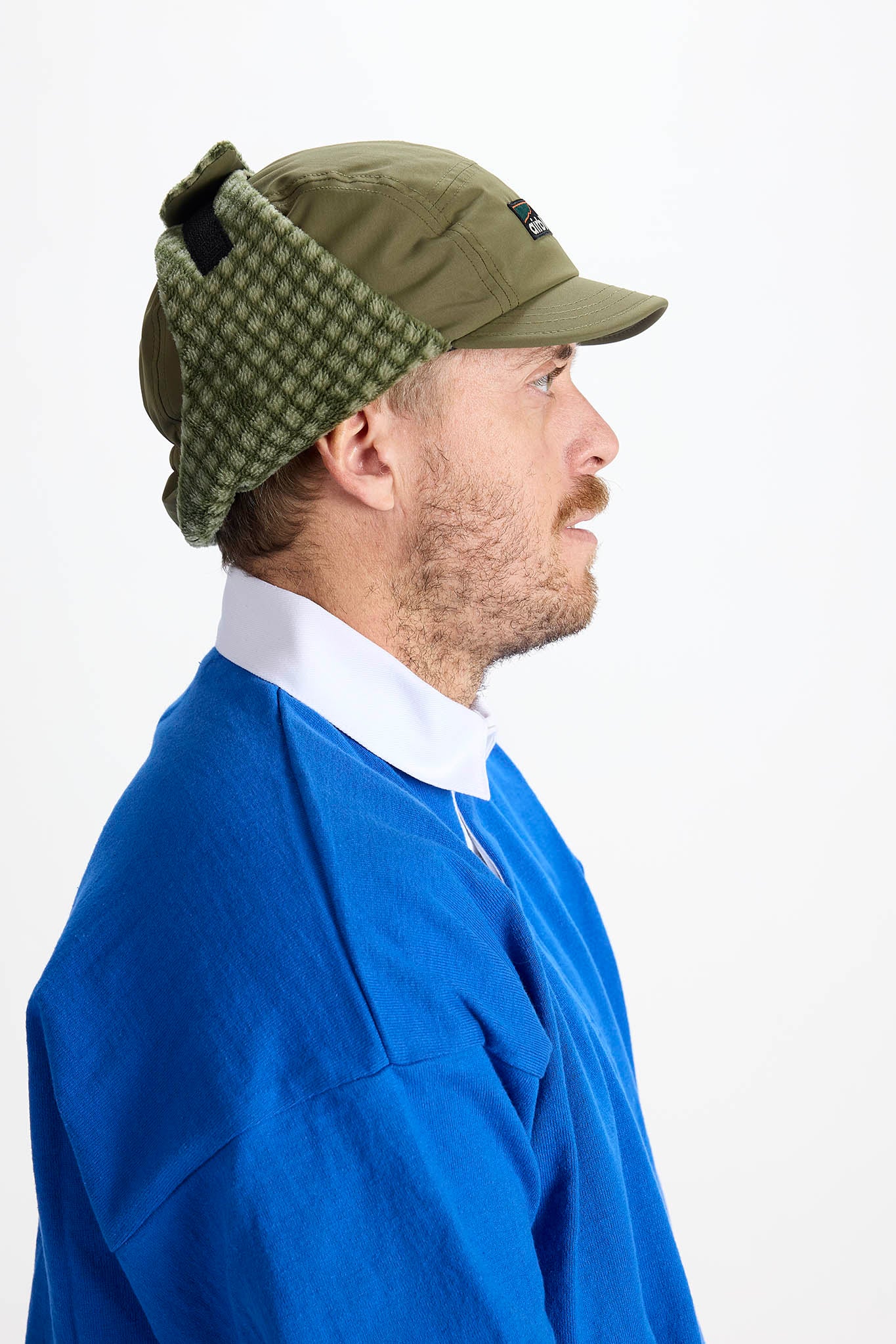 man in profile wearing a olive earflap hat