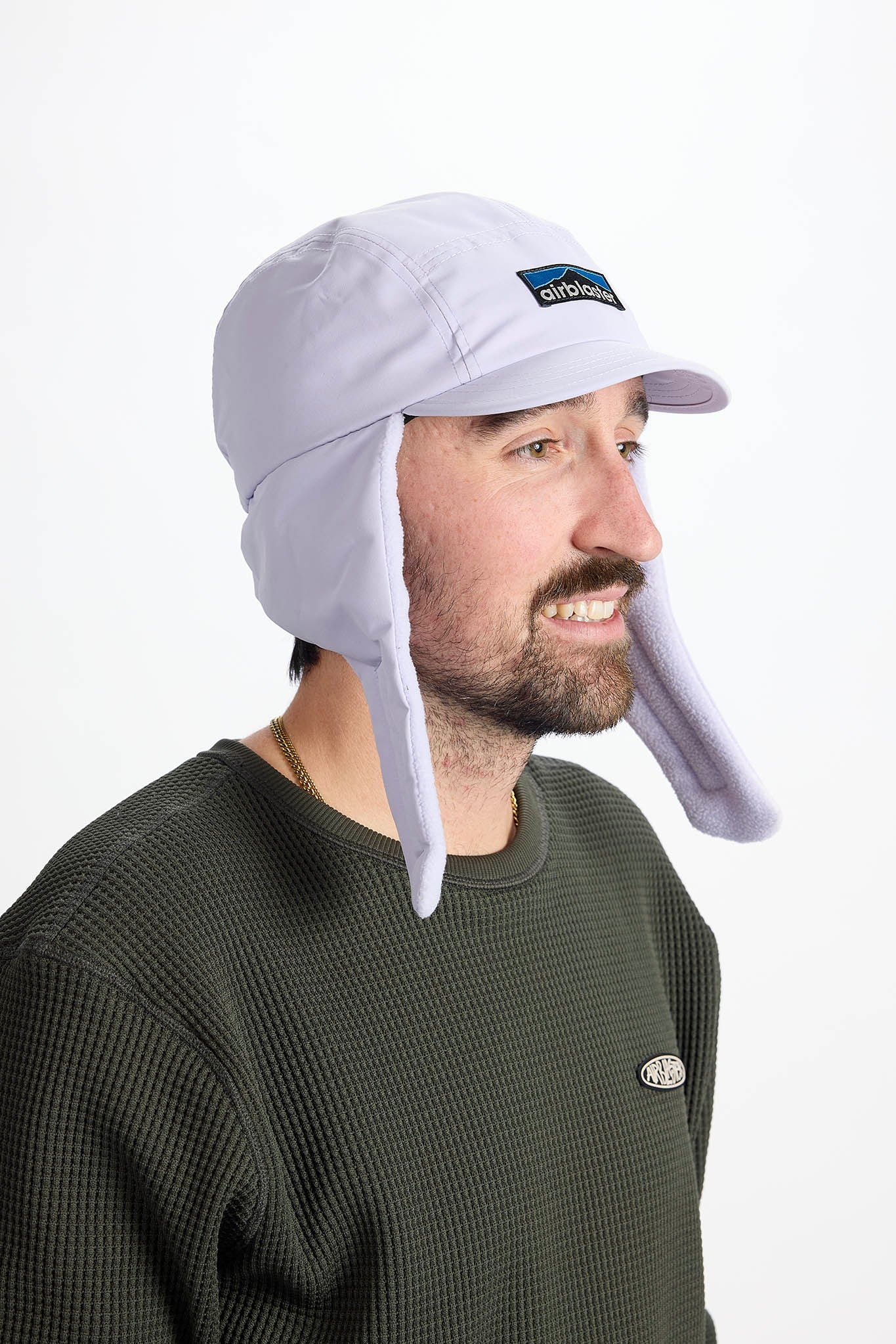 A man wearing a white wintery sun hat with ear flaps and a chin strap, on white background.