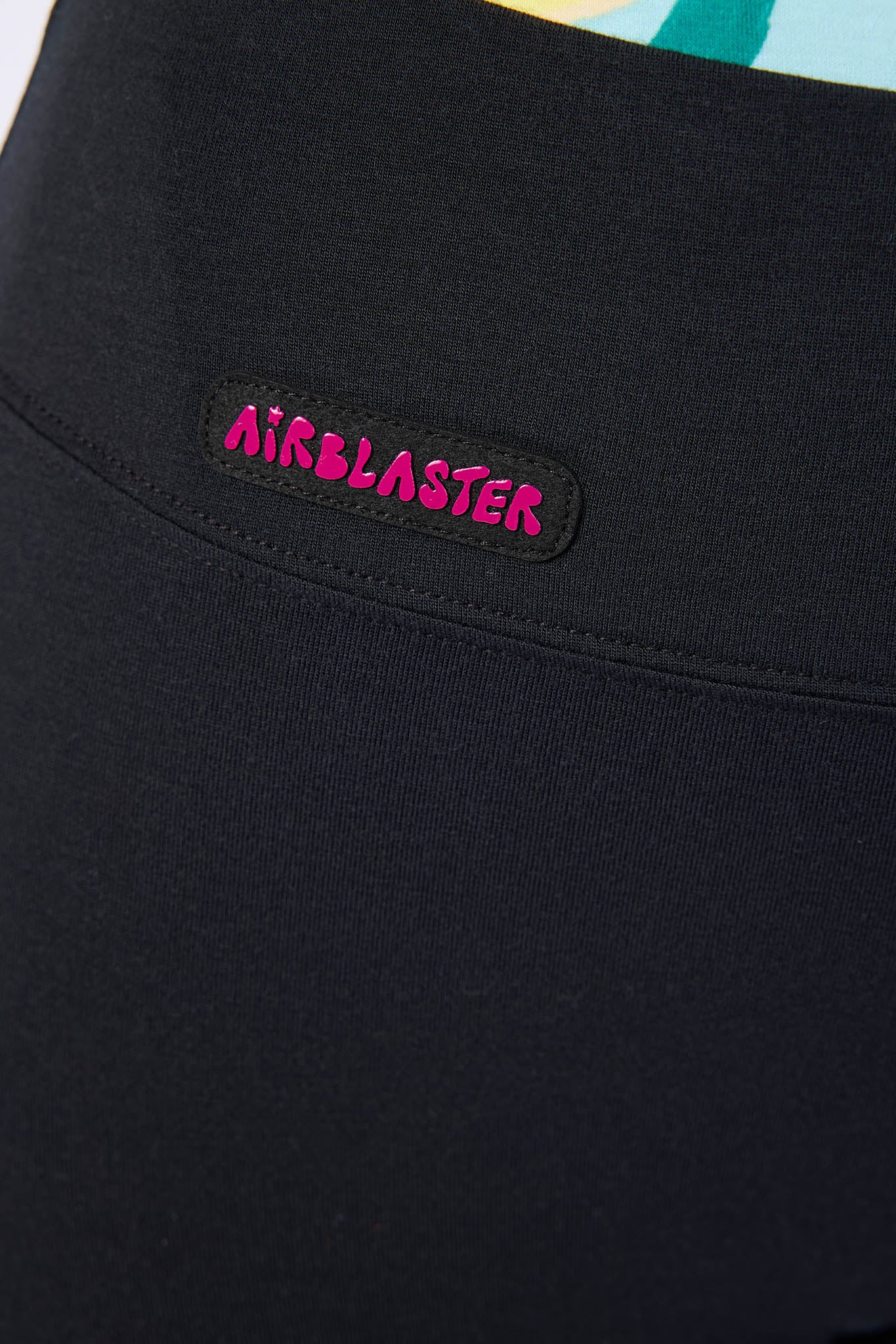 Close-up of a black garment featuring a rectangular black patch with the word 'AIRBLASTER' in bright pink lettering.