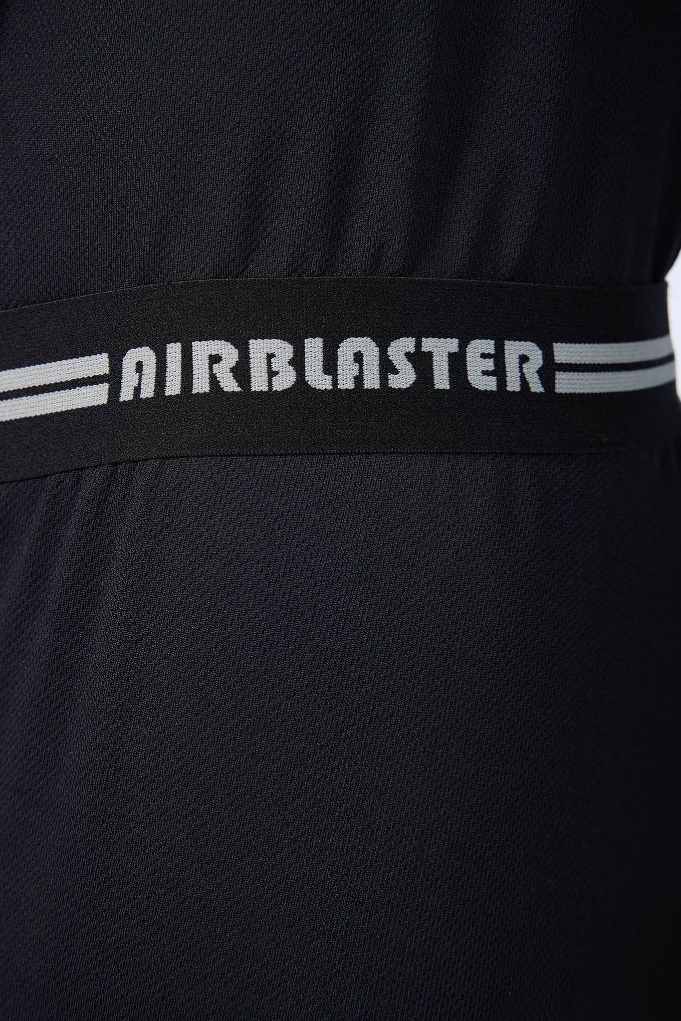 Close-up of a black textured athletic garment with a wide black waistband featuring the AIRBLASTER logo in white and two white stripes on each side.