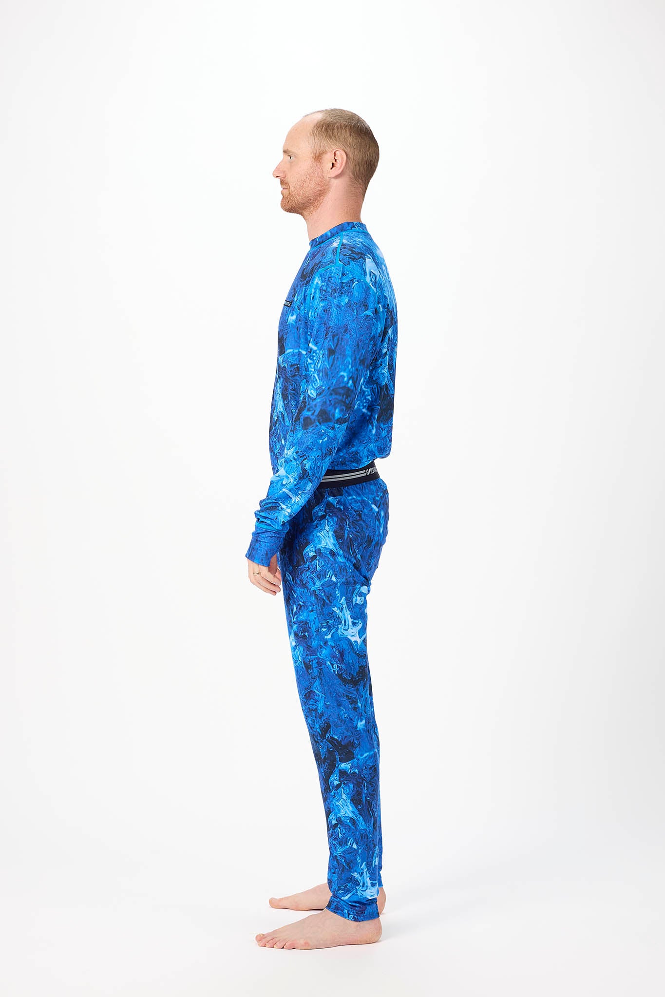 in side profile A man wearing a blue and black abstract patterned long-sleeve base layer set, standing against a plain white studio background.