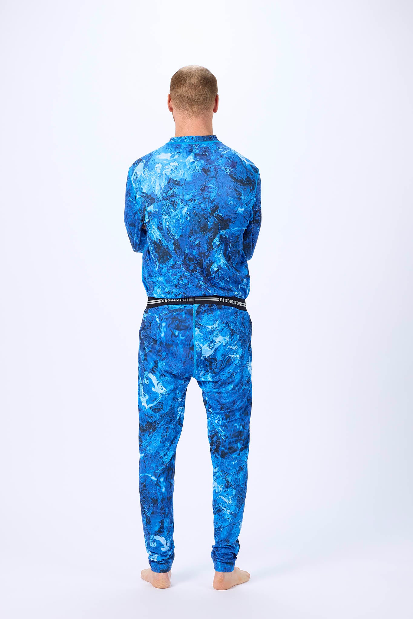 viewed from behind A man wearing a blue and black abstract patterned long-sleeve base layer set, standing against a plain white studio background.