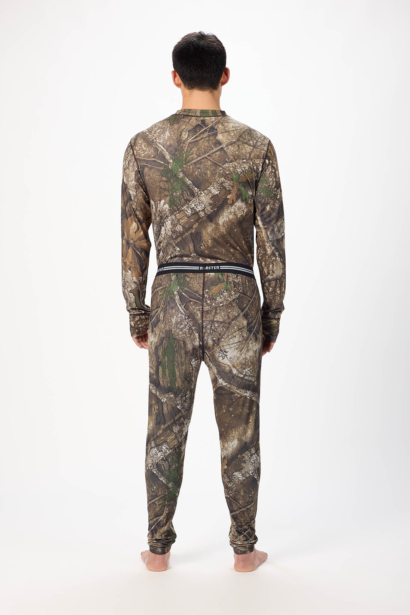 A man viewed from behind wearing a matching long-sleeve shirt and pants set in a woodland camouflage pattern, standing against a plain white studio background.