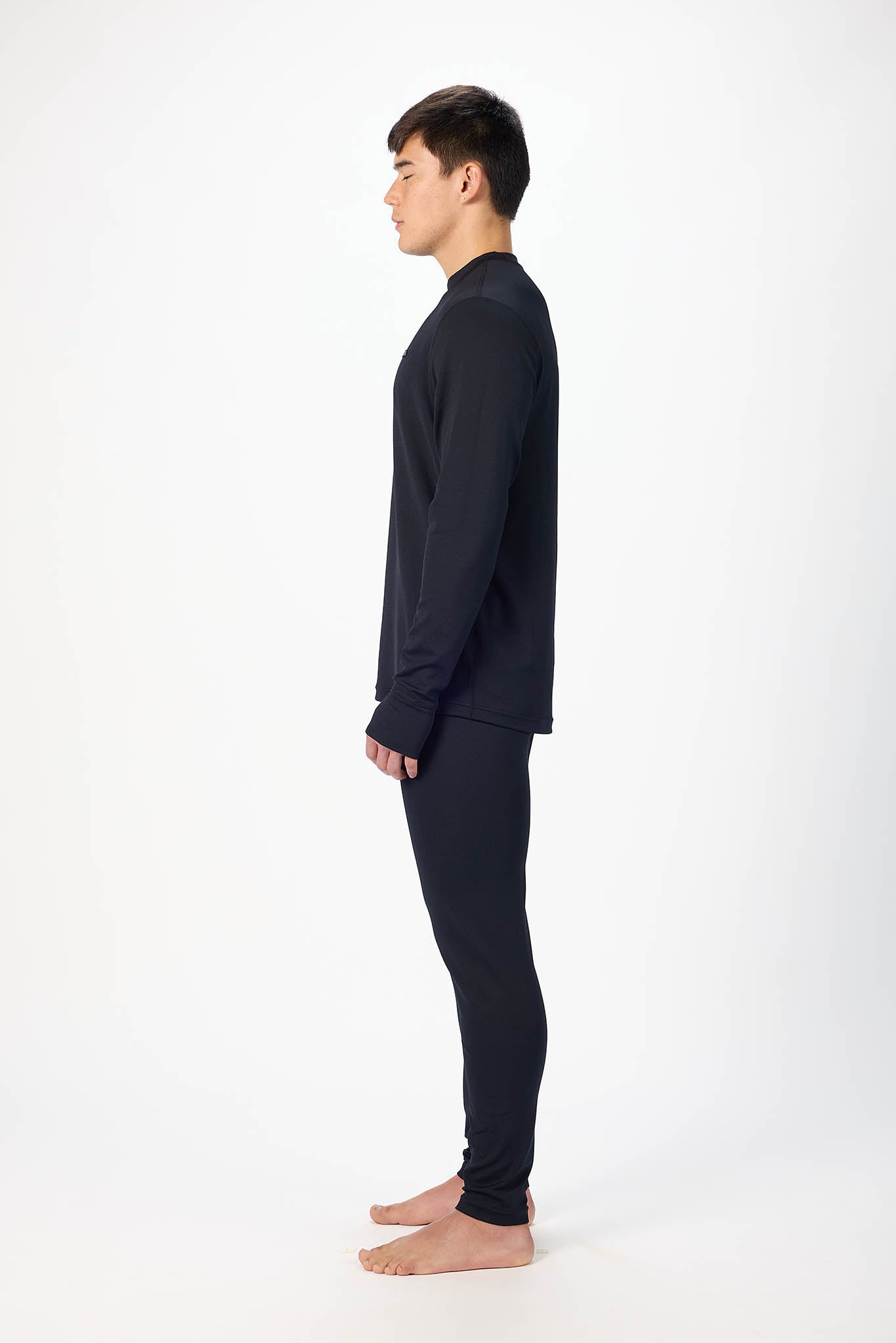 A man in a dark navy long-sleeve top and matching dark pants, shown in profile against a plain white studio background.