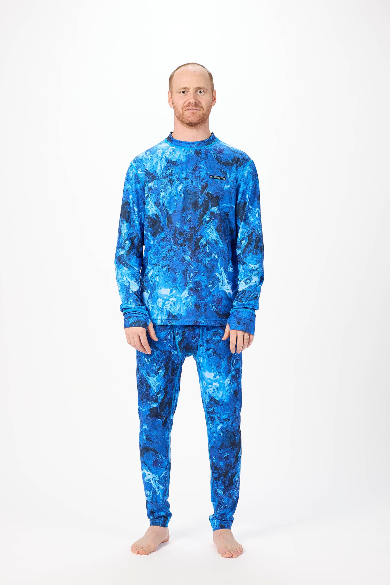 A man modeling a matching two-piece lounge set with a blue and black abstract watercolor pattern, consisting of a long-sleeve top and jogger pants, against a plain white studio background.