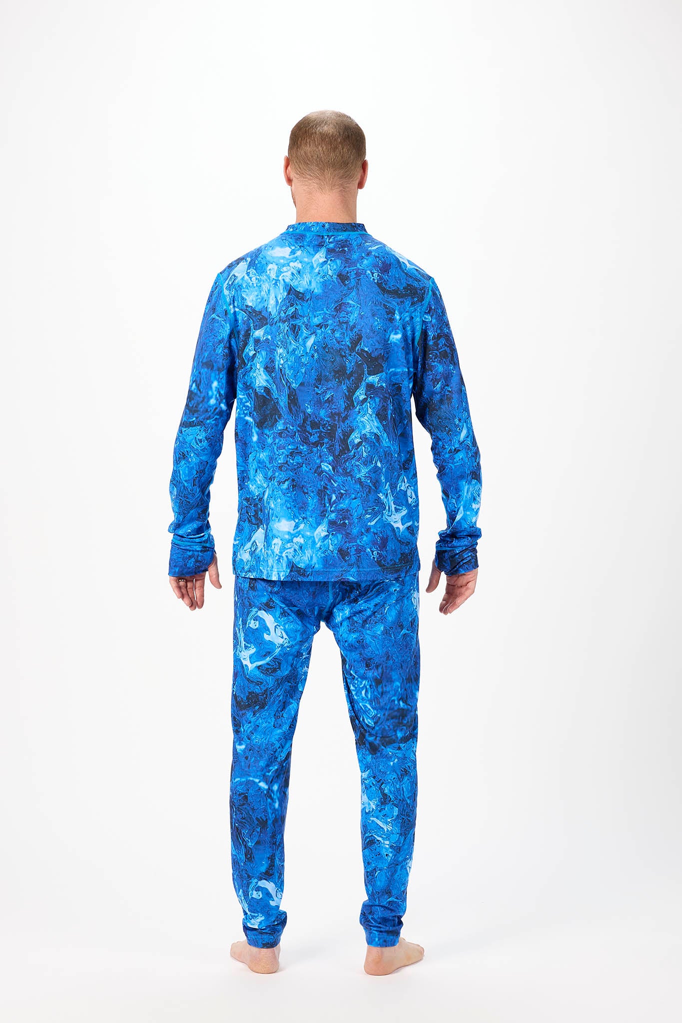 A man viewed from behind wearing a matching long-sleeve top and pants pajama set with a blue and black abstract marble pattern, standing against a white studio background.