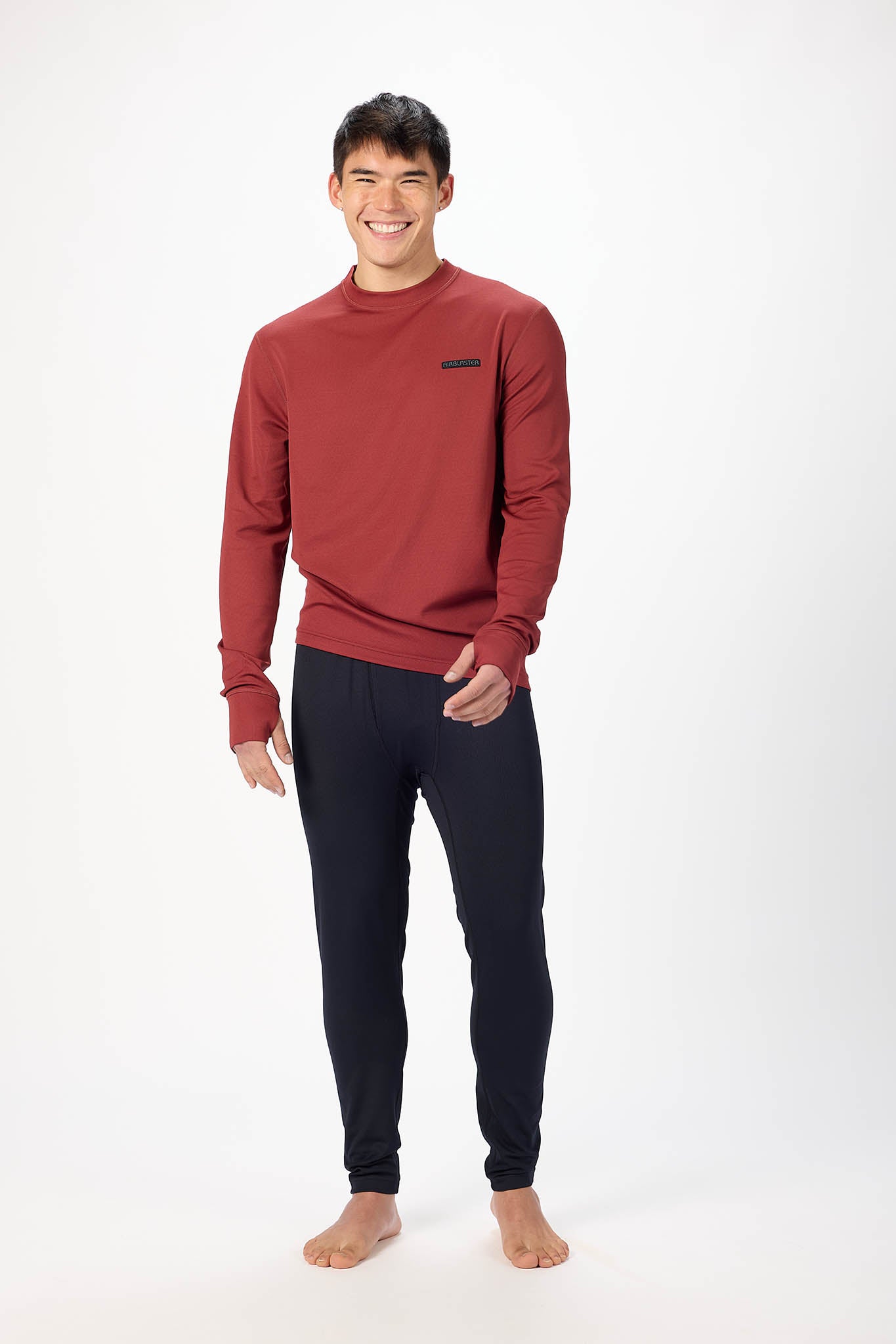A man modeling a rust red long-sleeve crewneck sweatshirt and dark navy jogger pants against a plain white studio background.