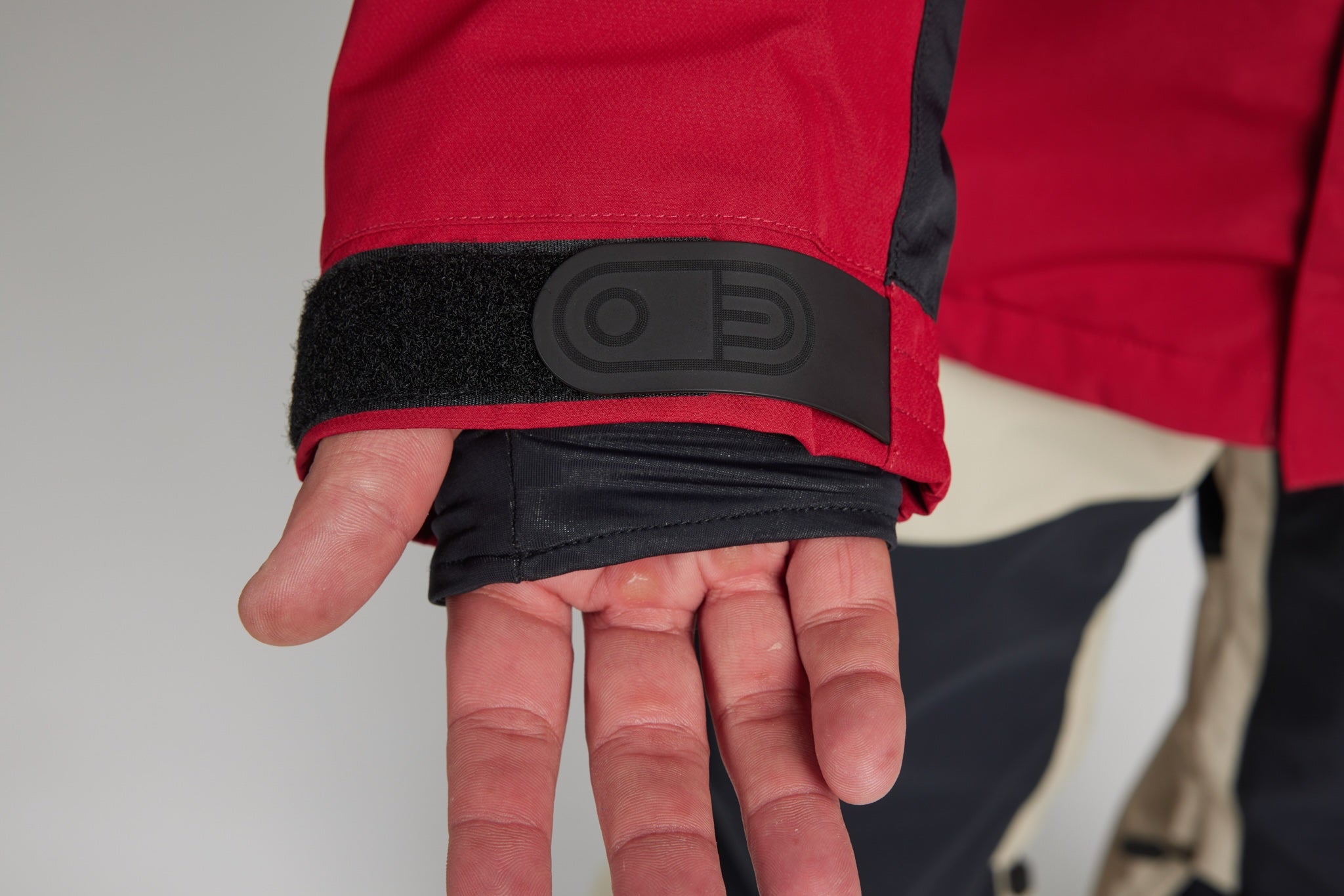 Close-up of a person's hand wearing a black insulated wrist warmer under a red and black jacket cuff, showing a molded black control panel on the cuff.
