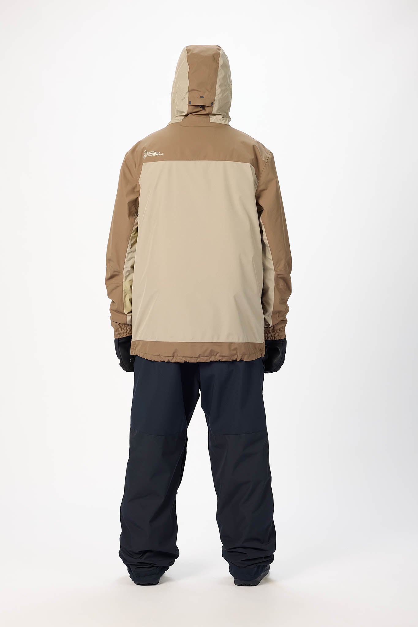 Person wearing a beige and brown snow jacket with black pants on a white background