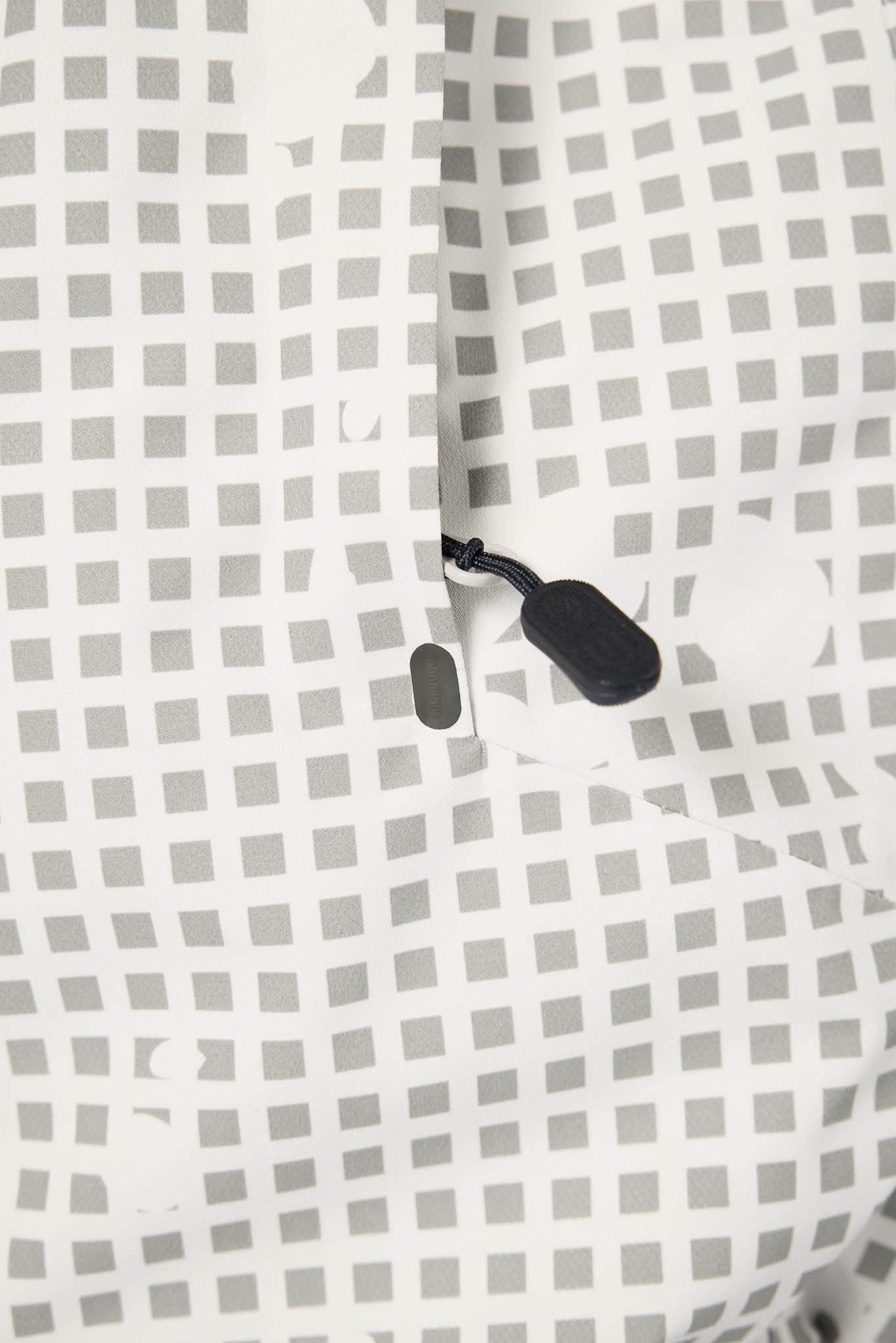 Close-up of a white garment with a gray geometric grid pattern and a black toggle detail.
