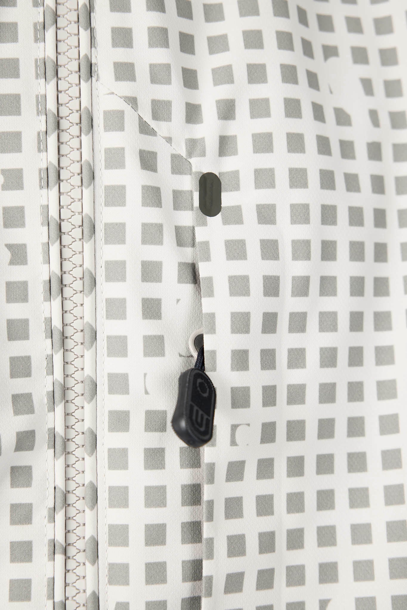 Close-up of a white and gray checkered patterned fabric with a black zipper pull and a black button detail.