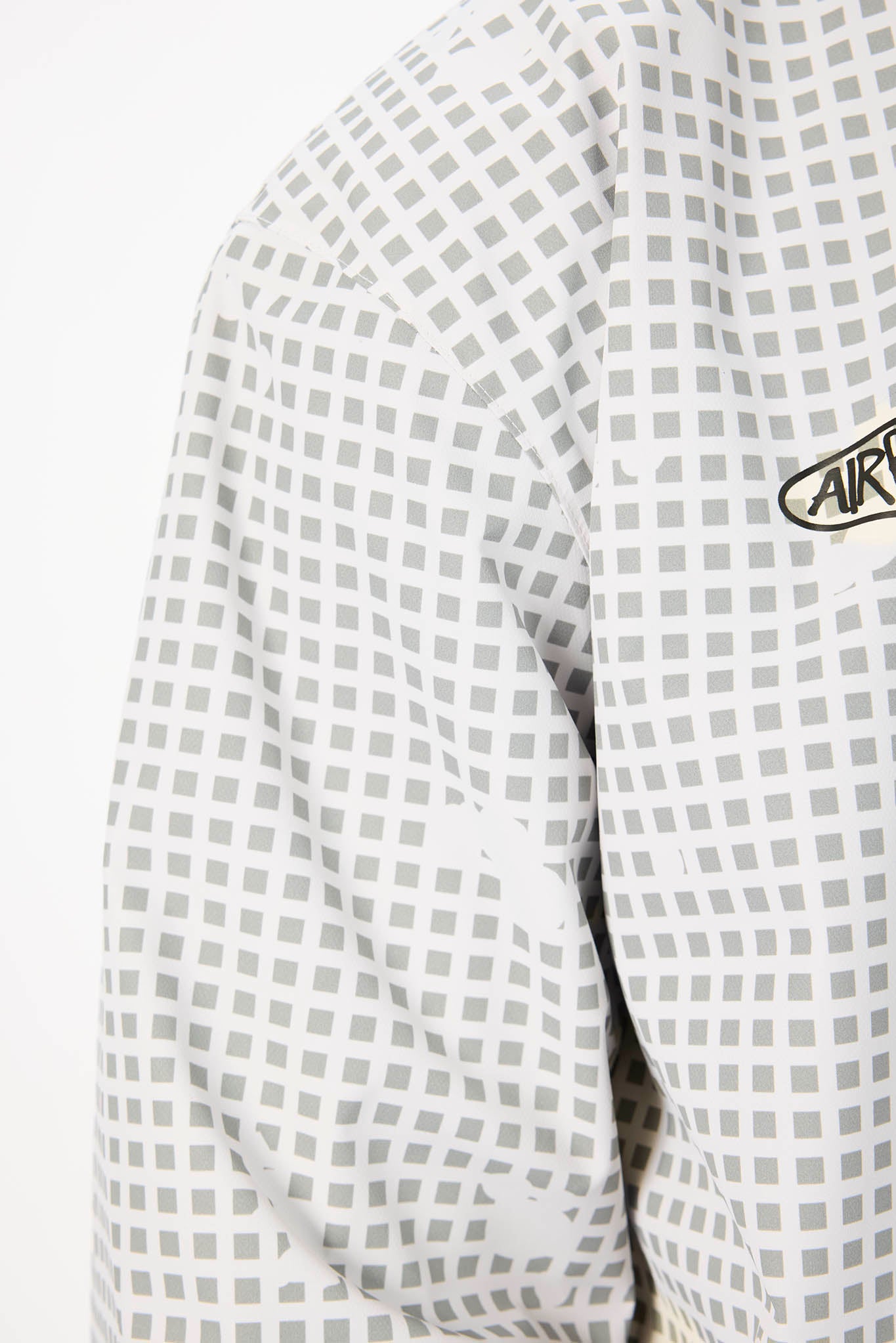 Close-up of a checkered shirt with a brand logo on the sleeve against a white background