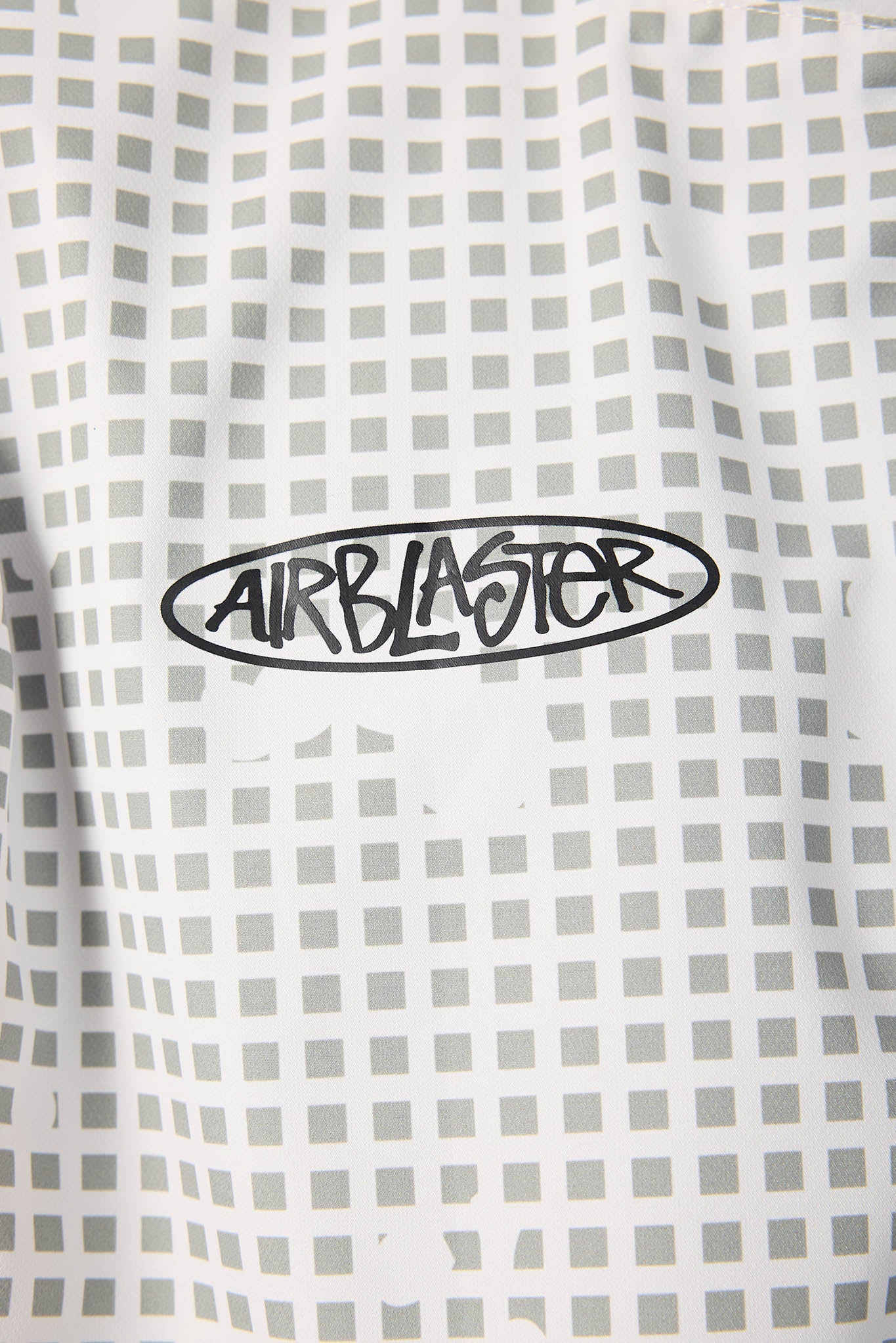 Close-up of a white shirt with a black 'AIRBLASTER' logo on a checkered pattern.