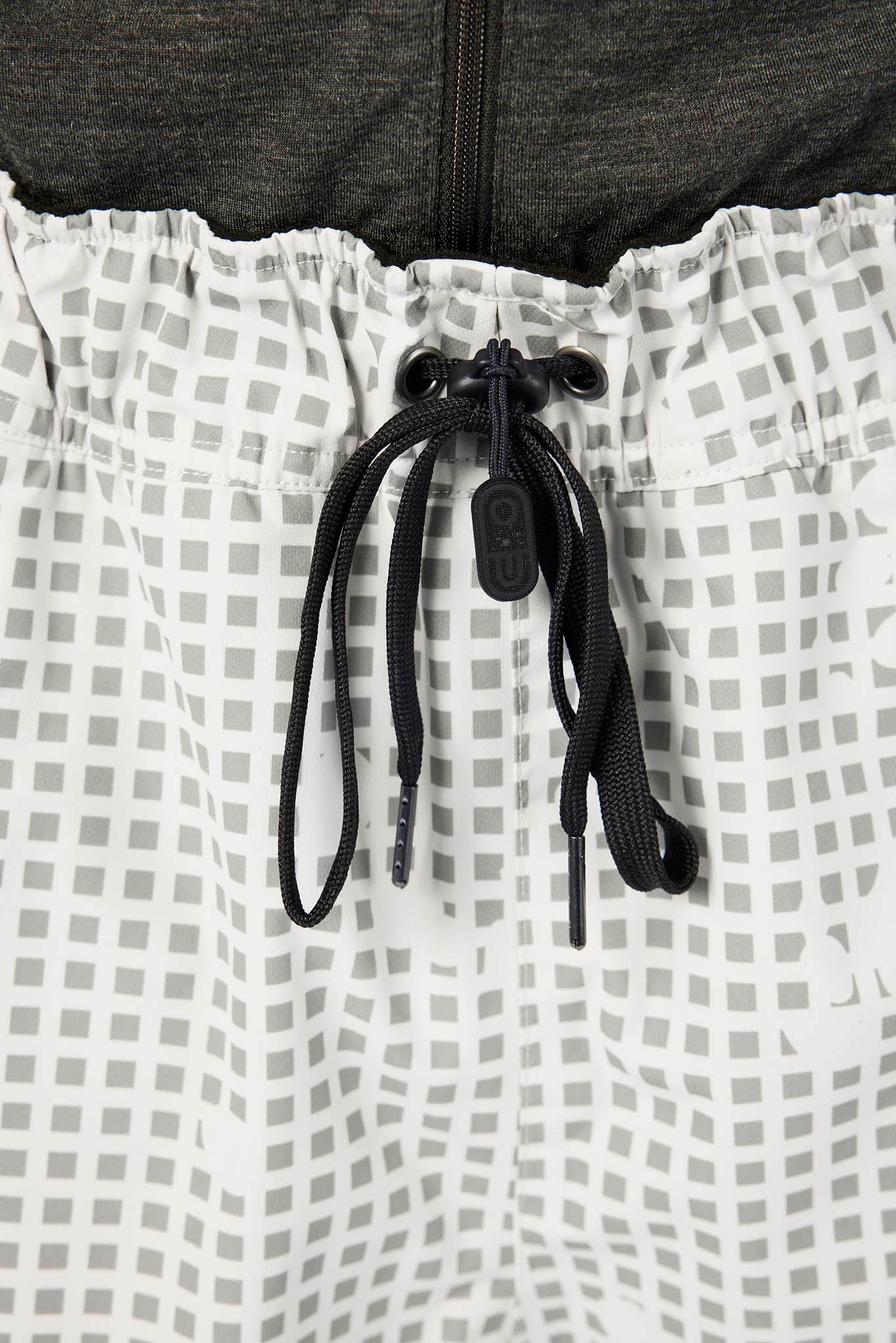 Close-up of white athletic shorts with a gray grid pattern, featuring a black drawstring and a dark gray zippered top underneath.