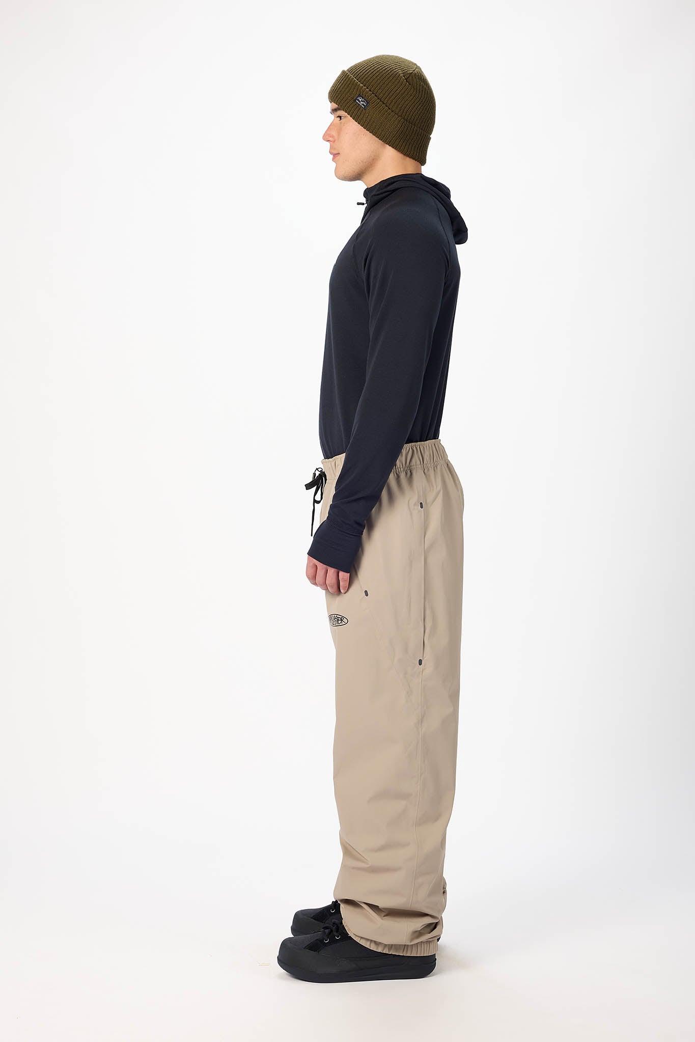 Person wearing a dark jacket, beige pants, and a green beanie on a white background