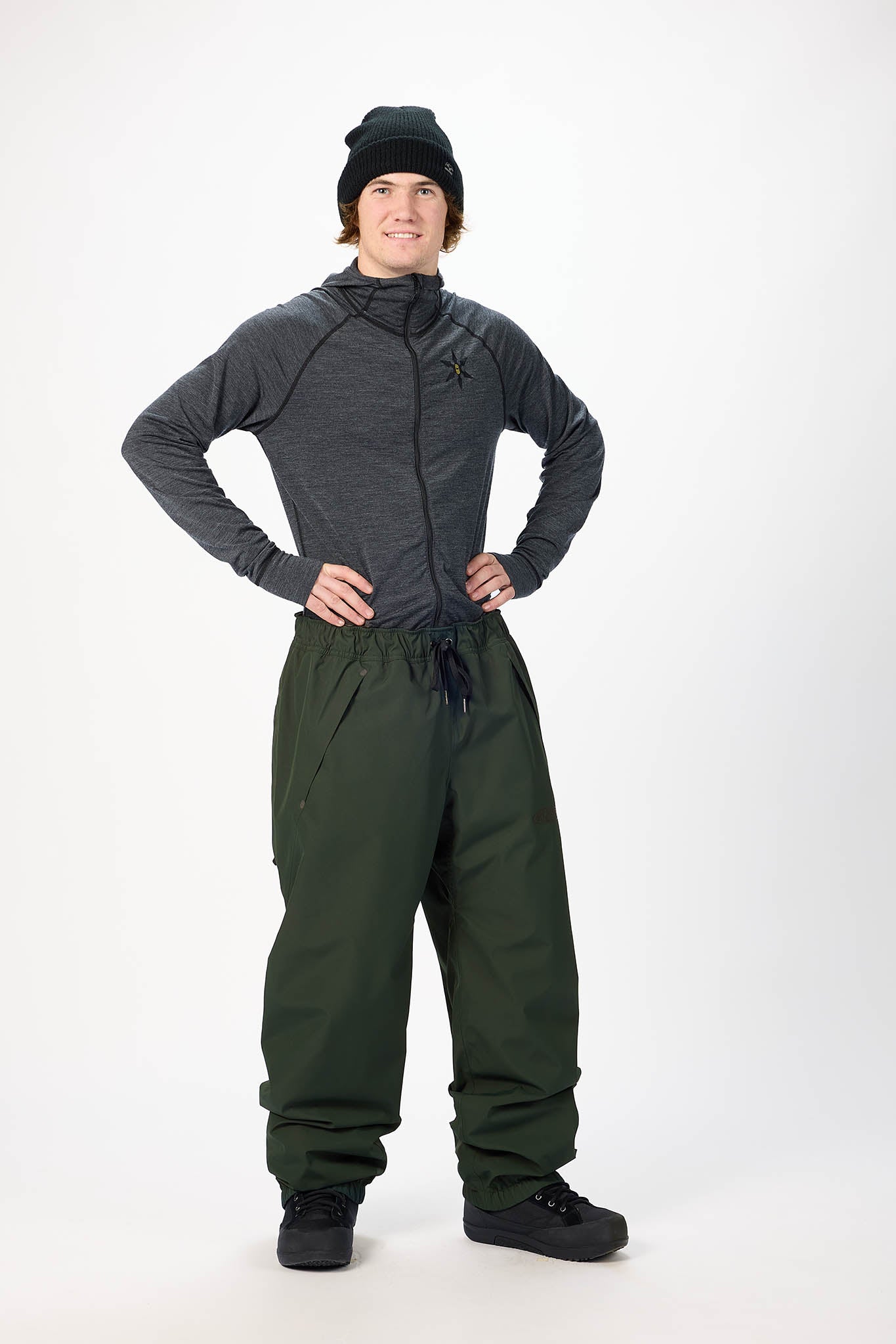 Person wearing a dark gray jacket and green snow pants on a white background