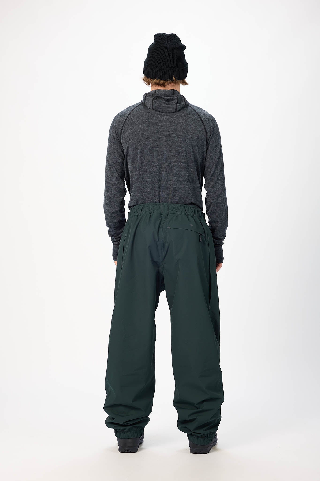 Person wearing a gray hoodie and green snow pants on a white background
