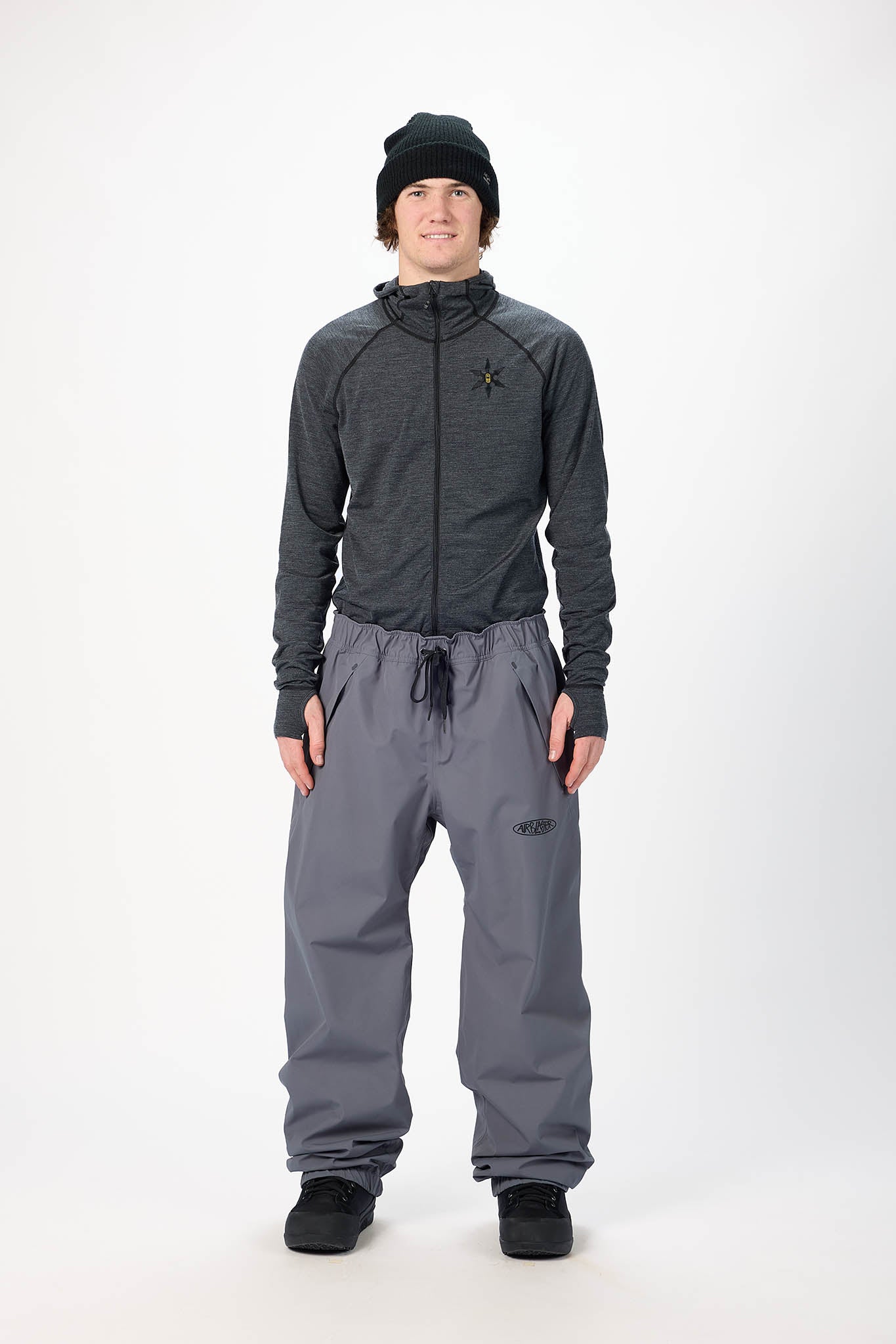 Person wearing a gray jacket and pants with a black beanie on a white background
