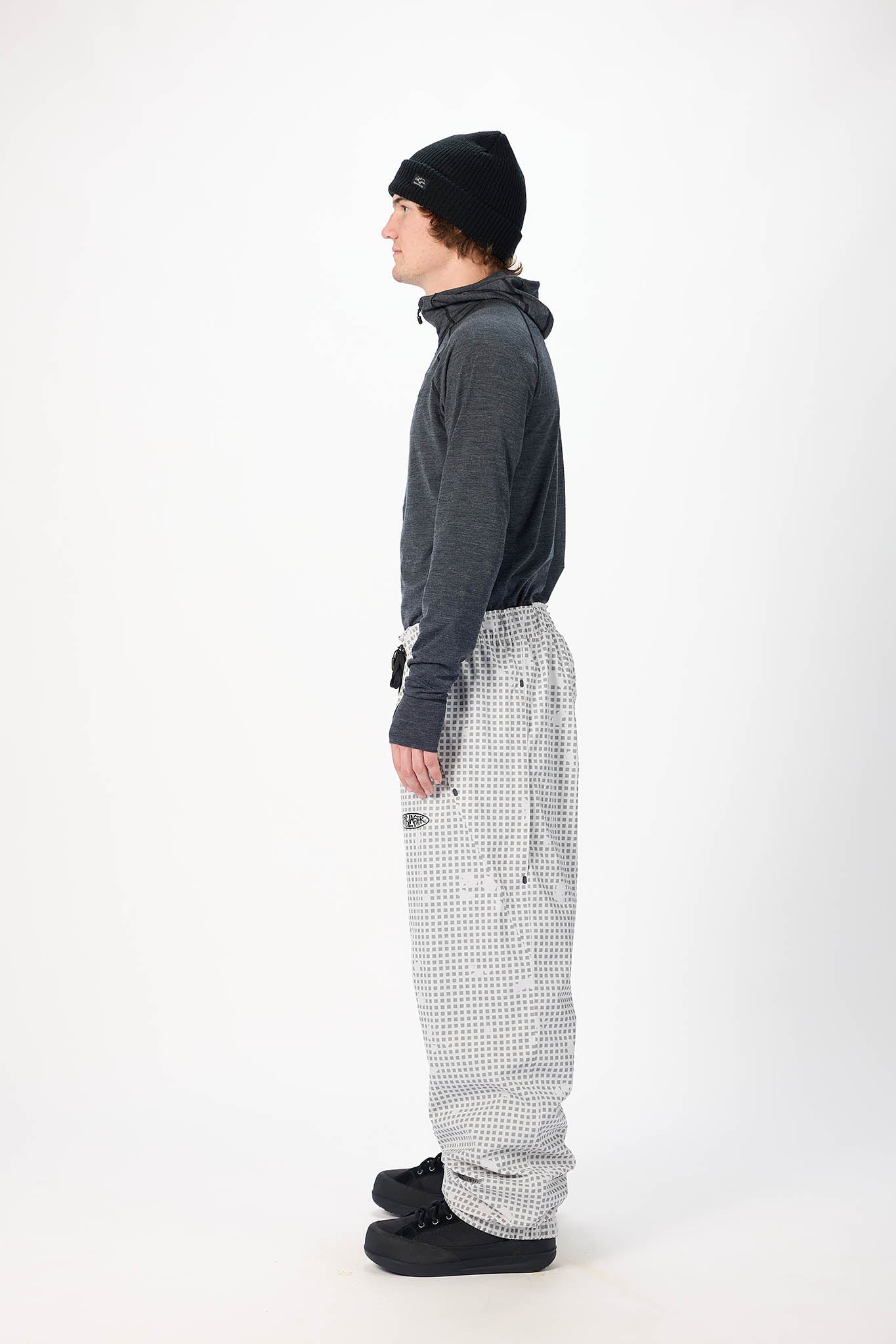 Person wearing a dark gray hoodie, black beanie, and checkered pants on a white background