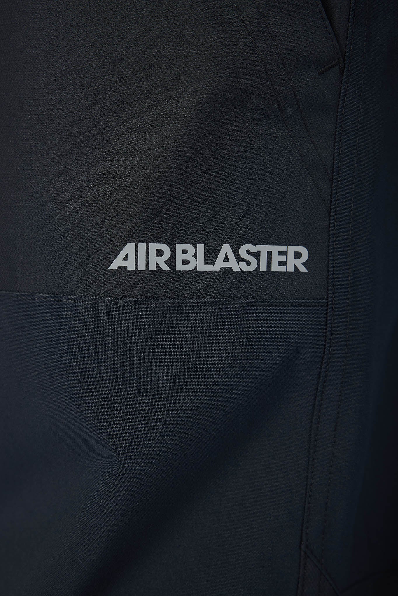 Close-up of a black jacket with 'AIRBLASTER' logo on a dark background