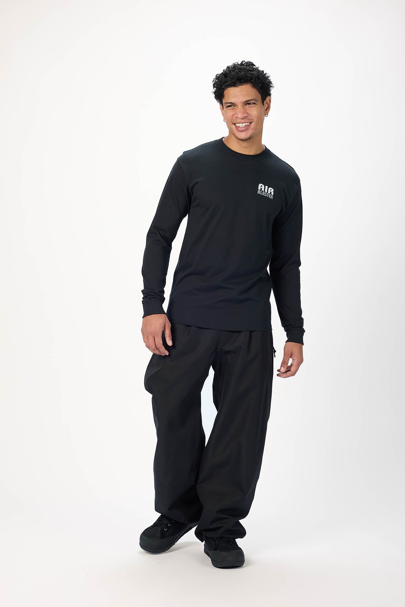 A man modeling a black long-sleeve crewneck shirt with a small white AIR logo on the left chest, paired with black cargo pants and black sneakers, against a plain white studio background.