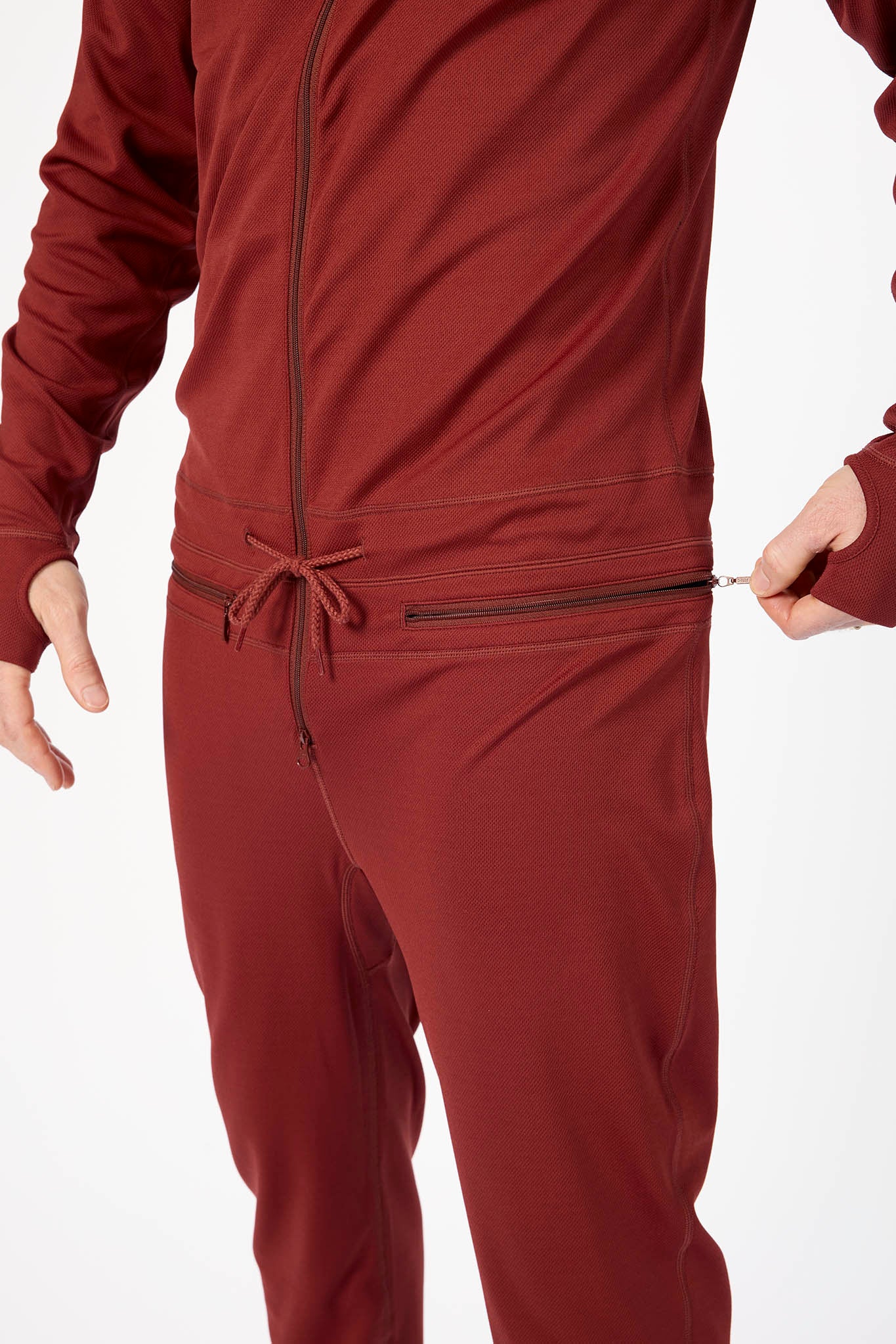 A close-up of a person wearing a matching burgundy zip-up jacket and jogger pants set, showing the waistband with a drawstring and a zippered pocket on the pants.