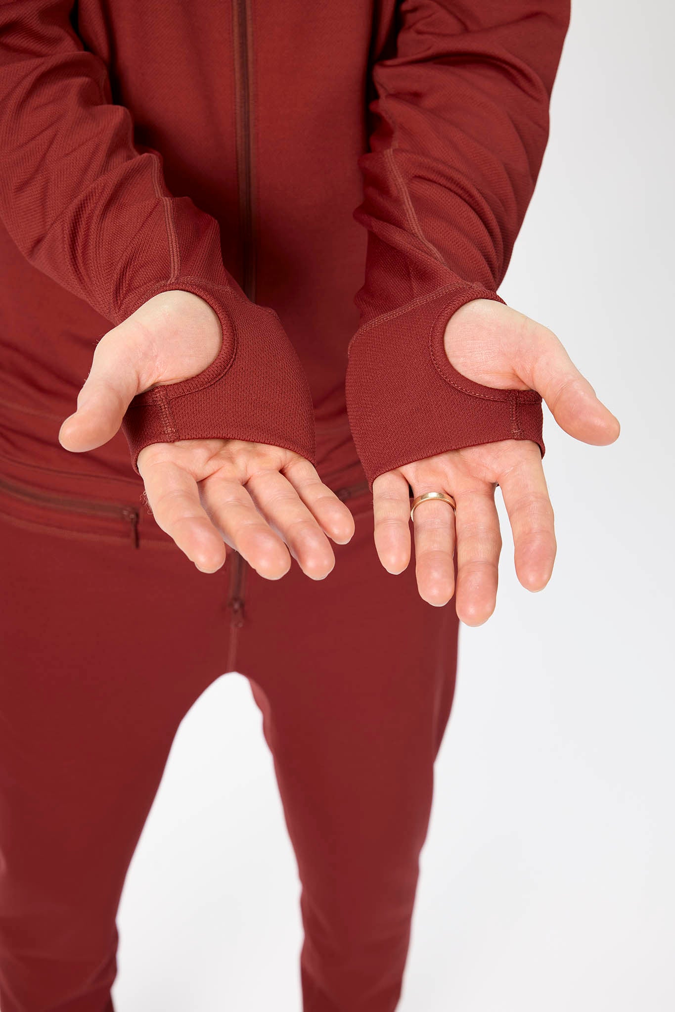 A close-up of a person wearing a matching burgundy zip-up jacket and pants, holding both hands forward to show the open cuff design of the jacket on a clean white background