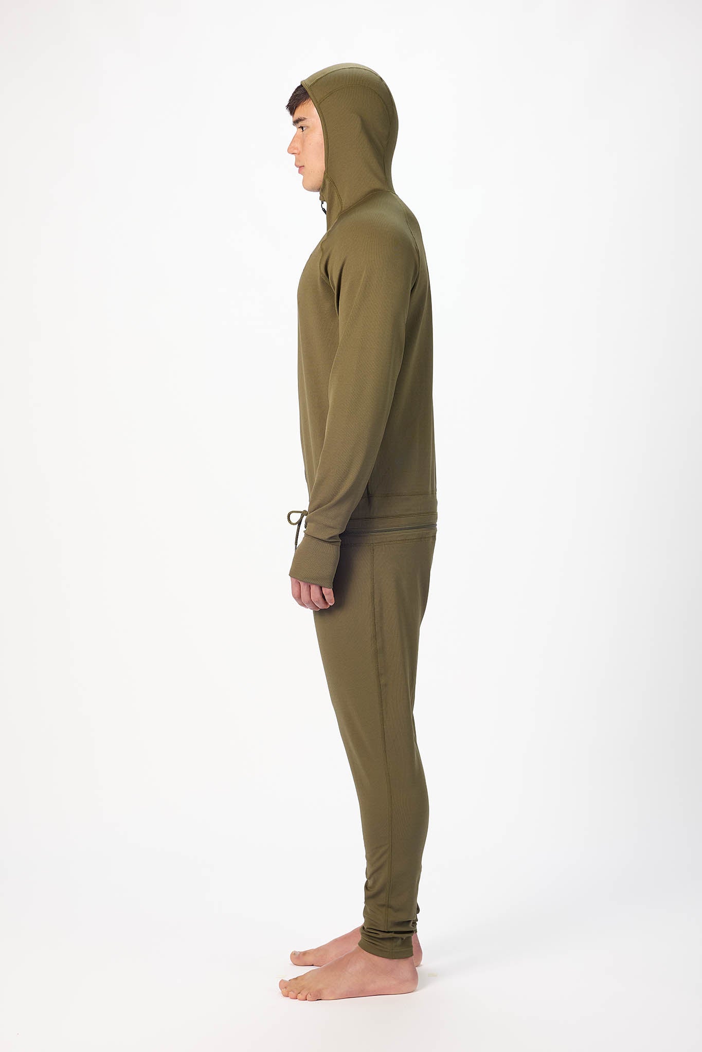 side profile of a man wearing a Olive onesie with a hooded with a zipper and jogger pants, standing against a plain white studio background.
