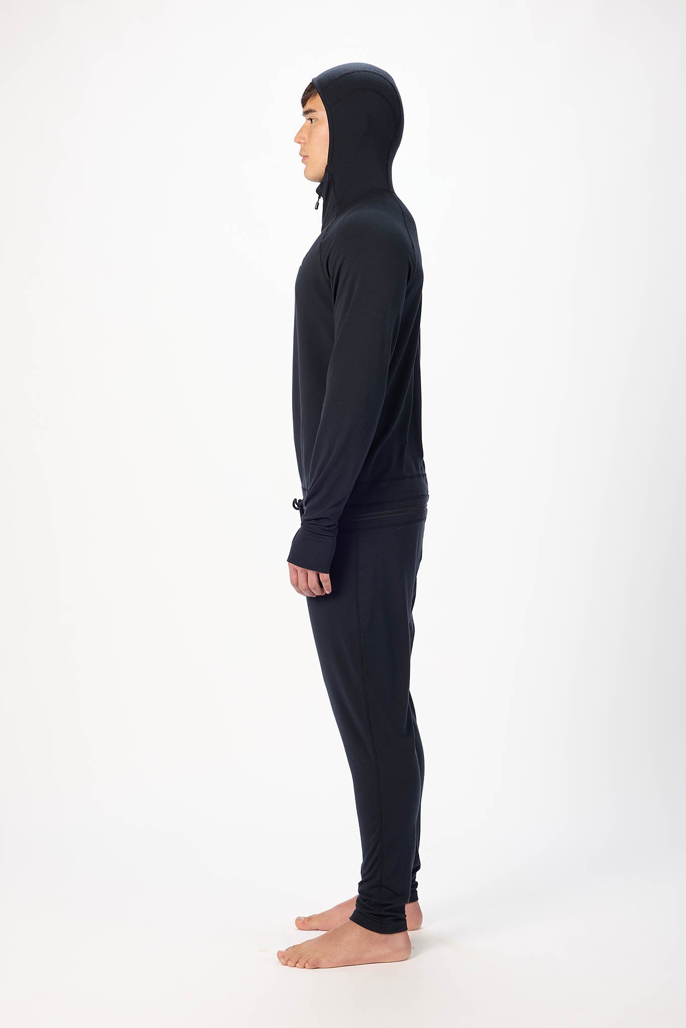in side view A man wearing a black onesie with a hooded zip-up jacket and jogger pants, standing against a plain white studio background.