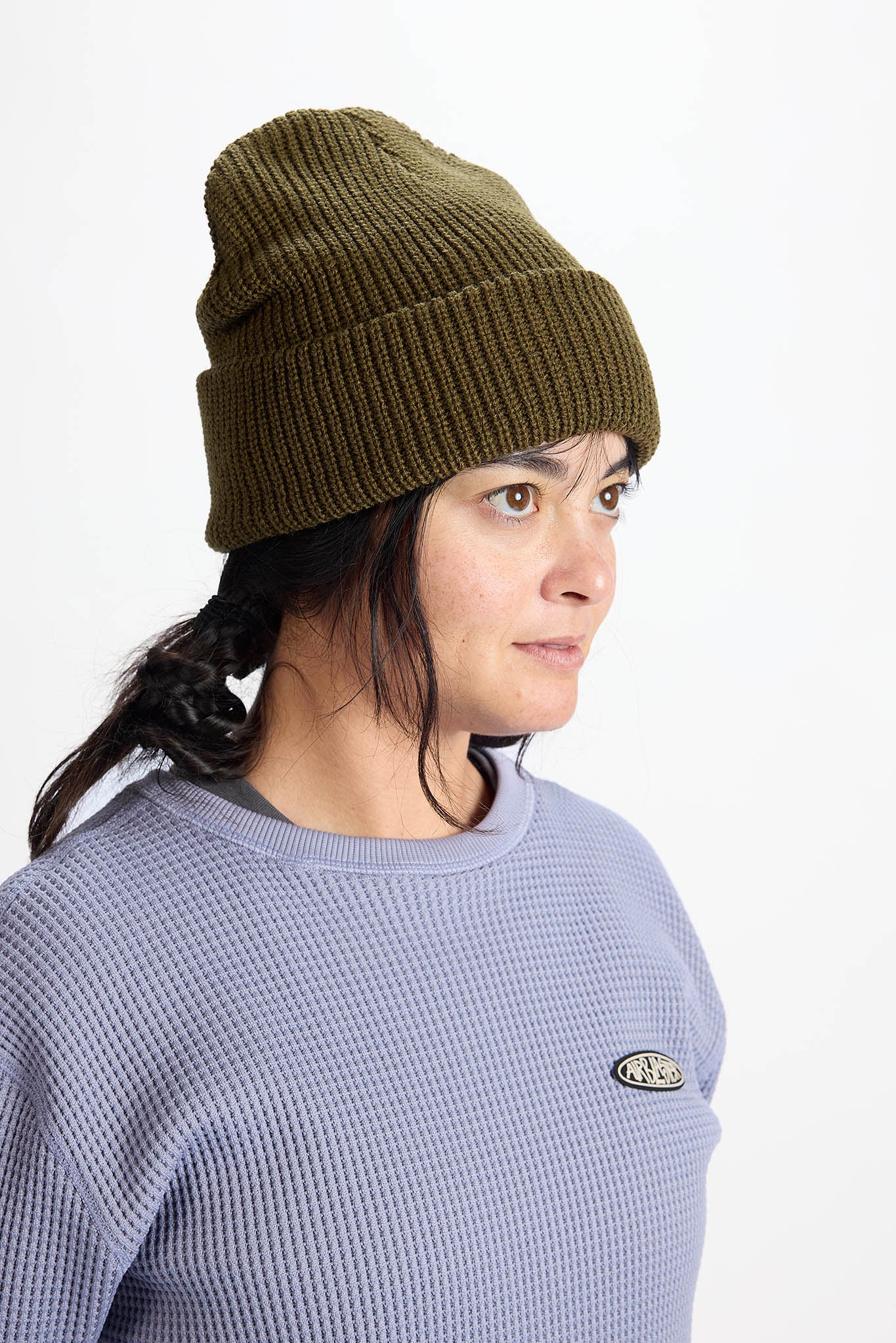 A woman in profile wearing a olive green ribbed knit beanie