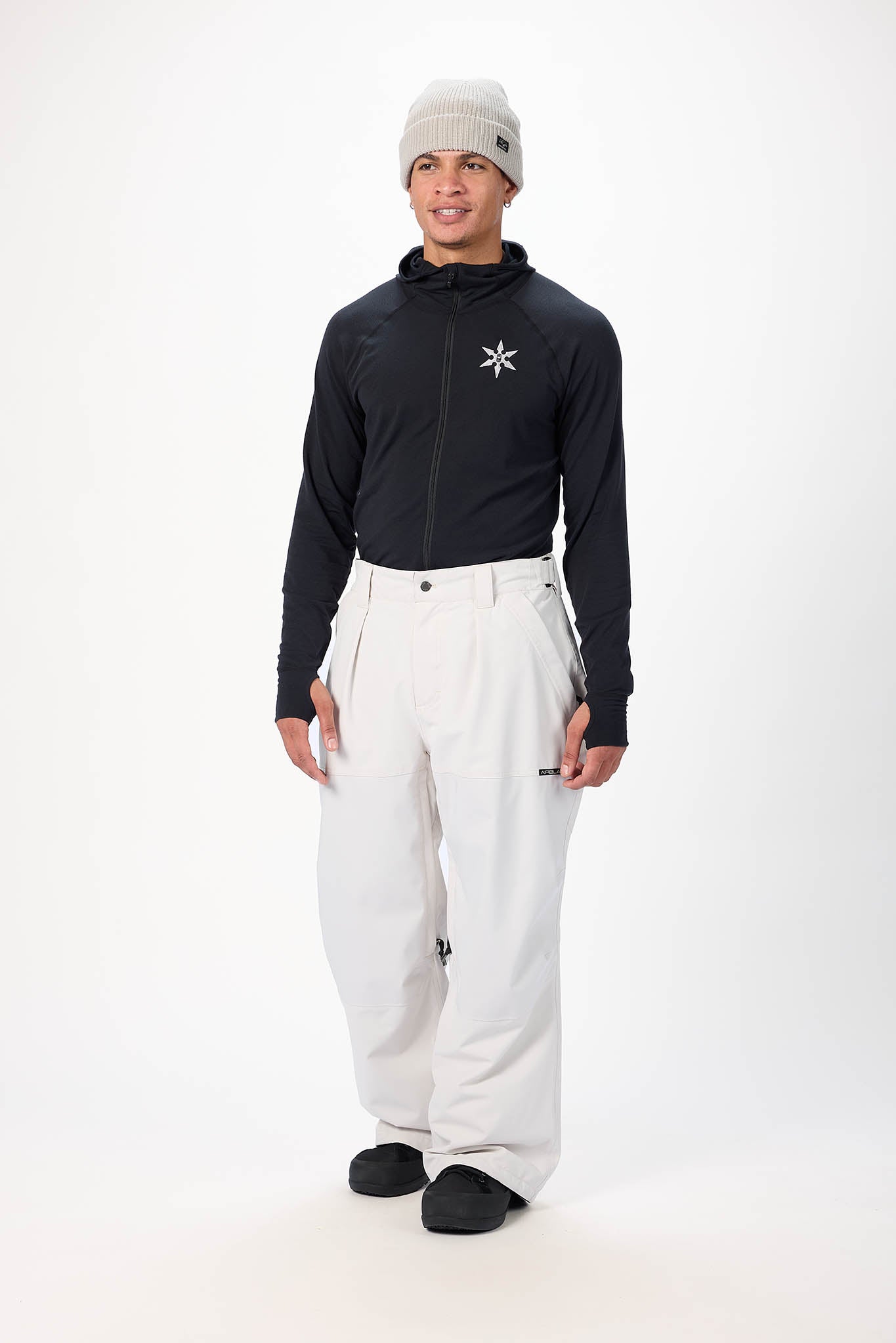 Person wearing a black jacket with a white logo and white pants on a white background