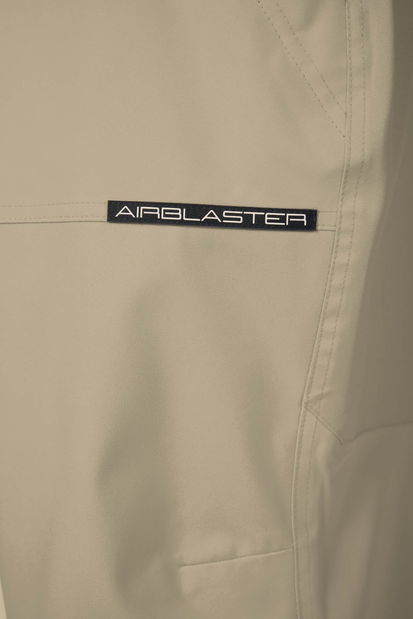 Close-up of beige pants with 'Airblaster' logo on a beige background
