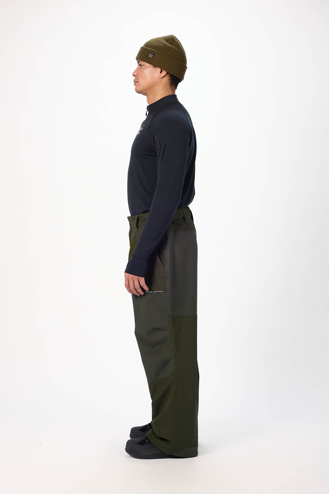 Person wearing a dark long-sleeve shirt, green pants, and a green beanie on a white background