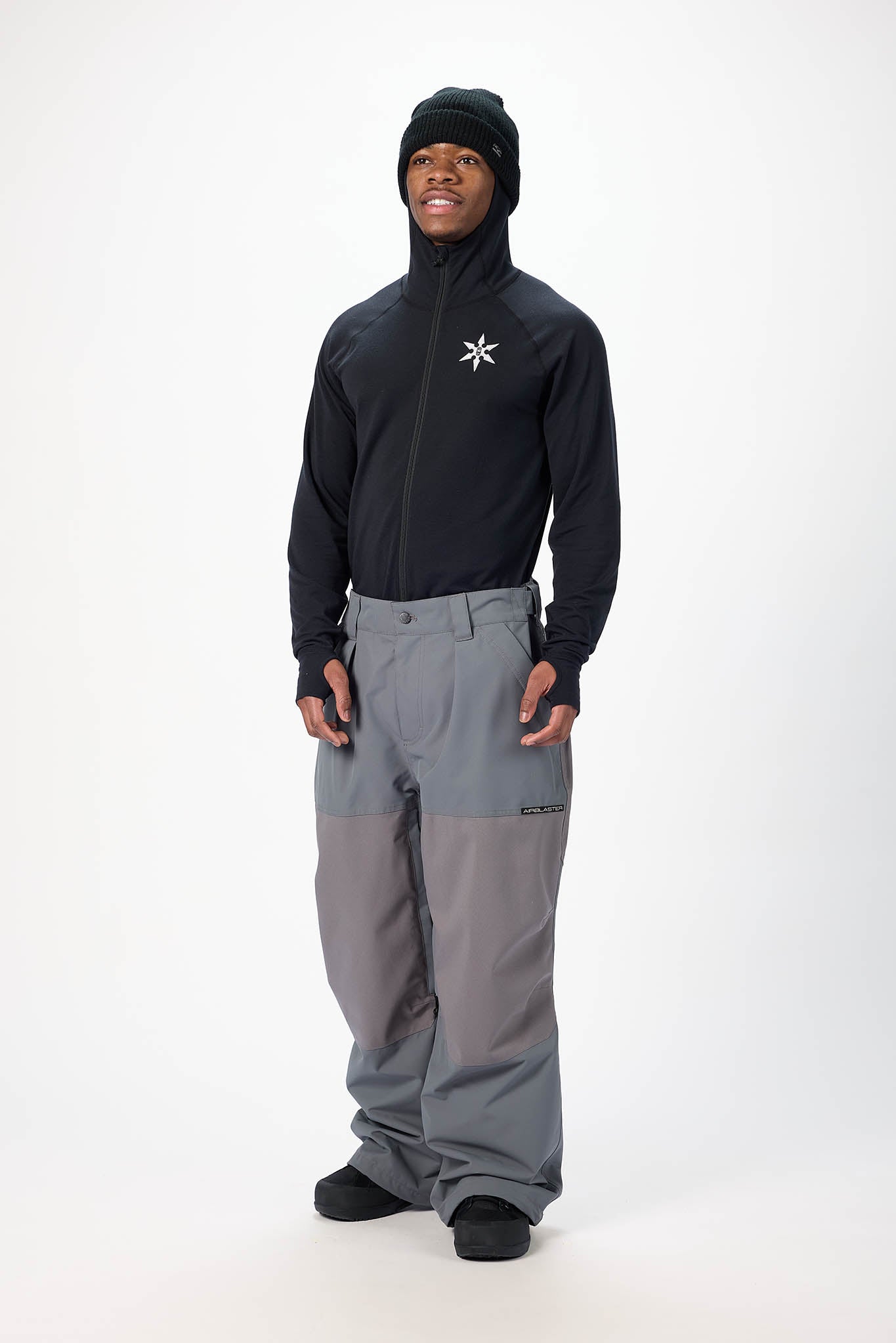 Person wearing a black jacket with a logo and gray pants on a white background