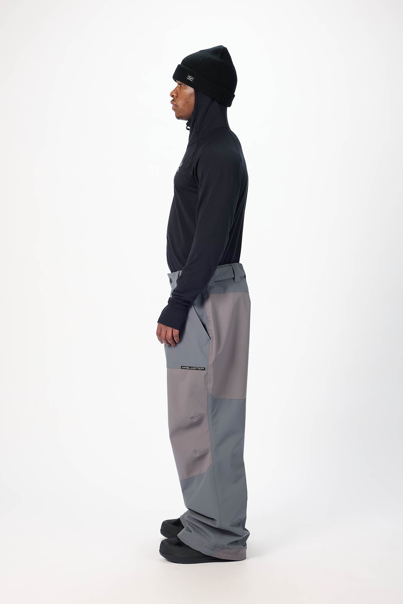 Person wearing a black jacket and gray pants on a white background