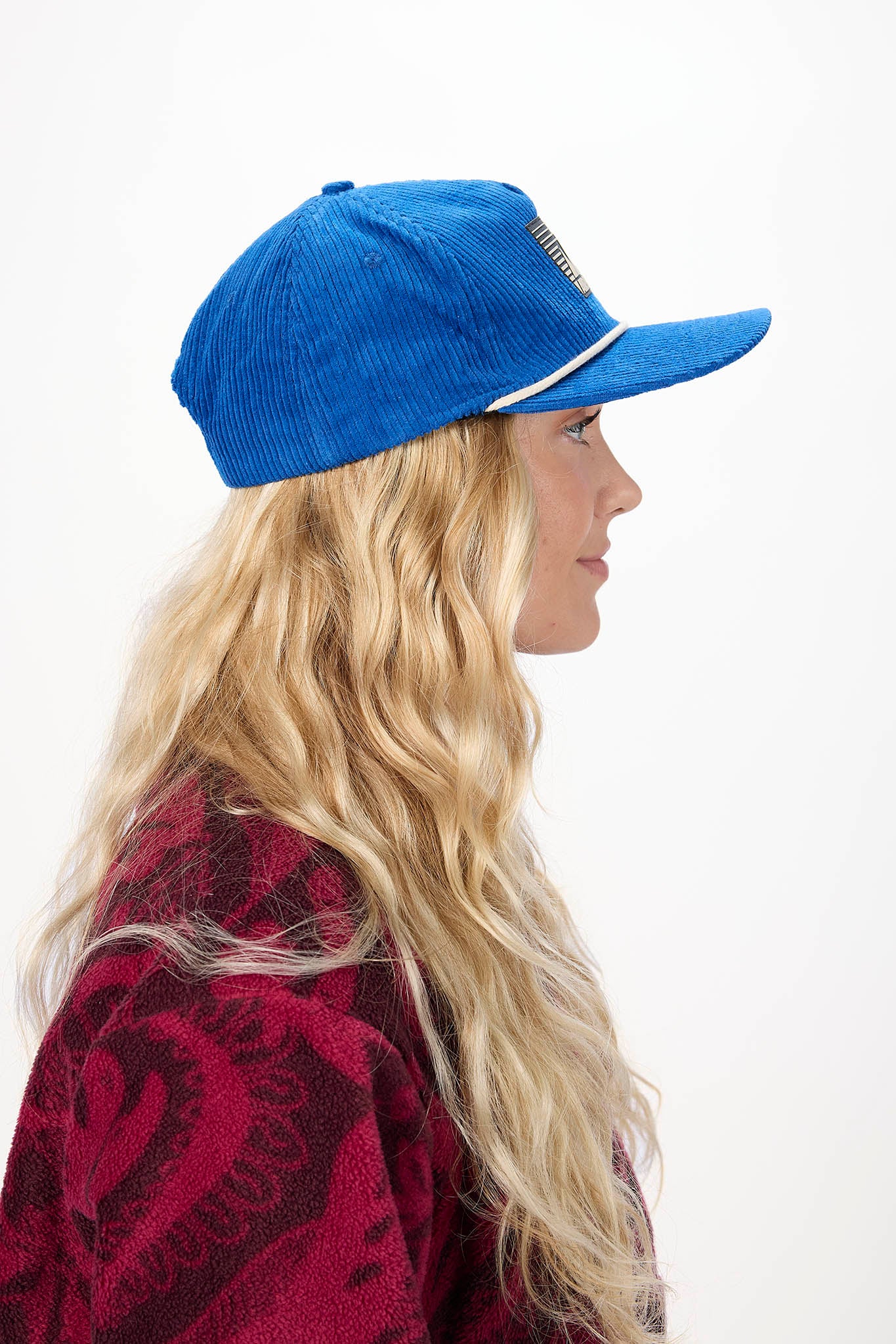 side profile A woman wearing a blue Airblaster baseball cap, photographed against a plain white background.