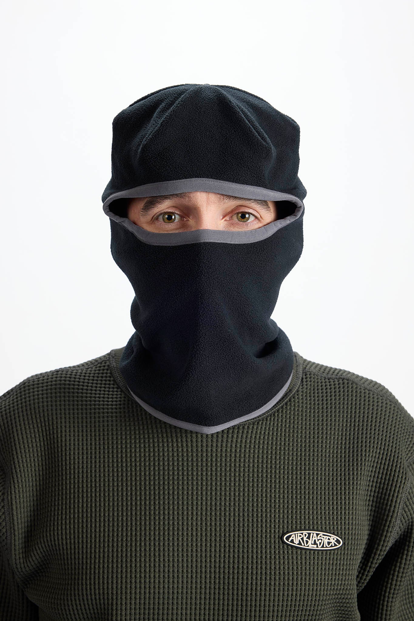 A person wearing a black balaclava face mask with gray trim over their eyes and mouth, paired with a dark green waffle-knit shirt.